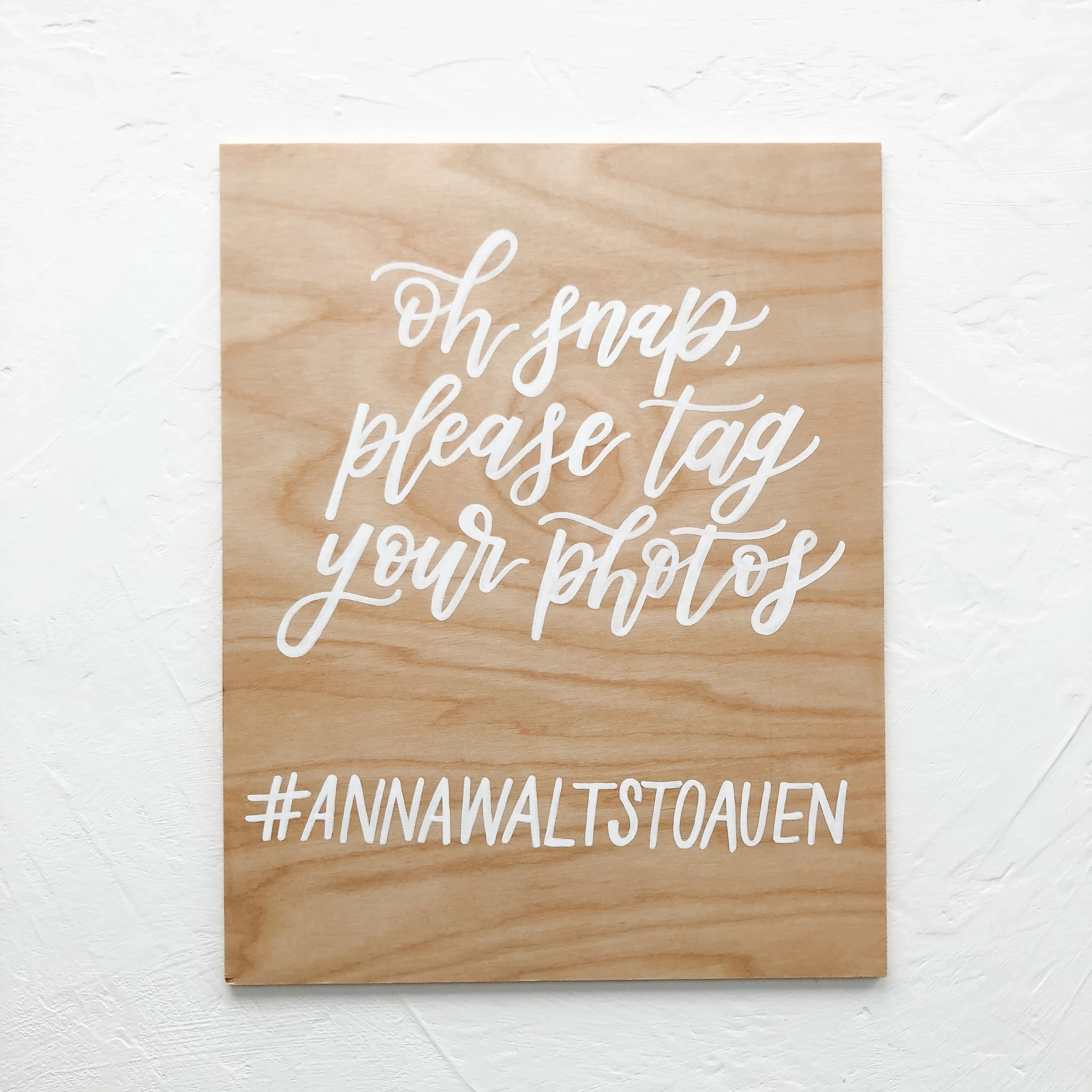 Encourage guests to share their social media photos with a playful, hand-lettered wooden hashtag sign. Crafted on light natural wood grain with crisp white calligraphy script that reads "Oh snap, please tag your photos," this custom easel sign offers