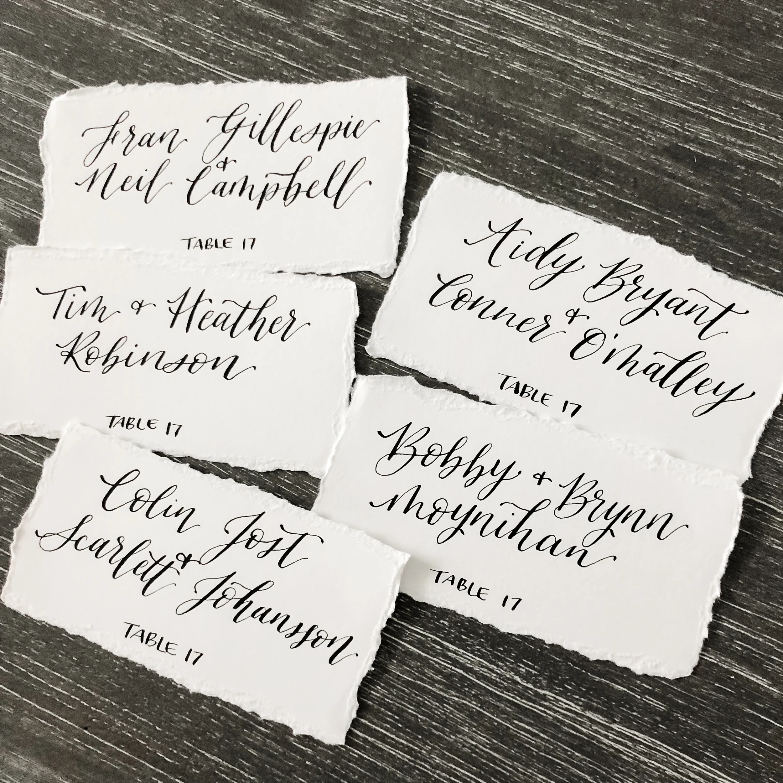 Deckled edge white paper wedding escort cards with classic black calligraphy.