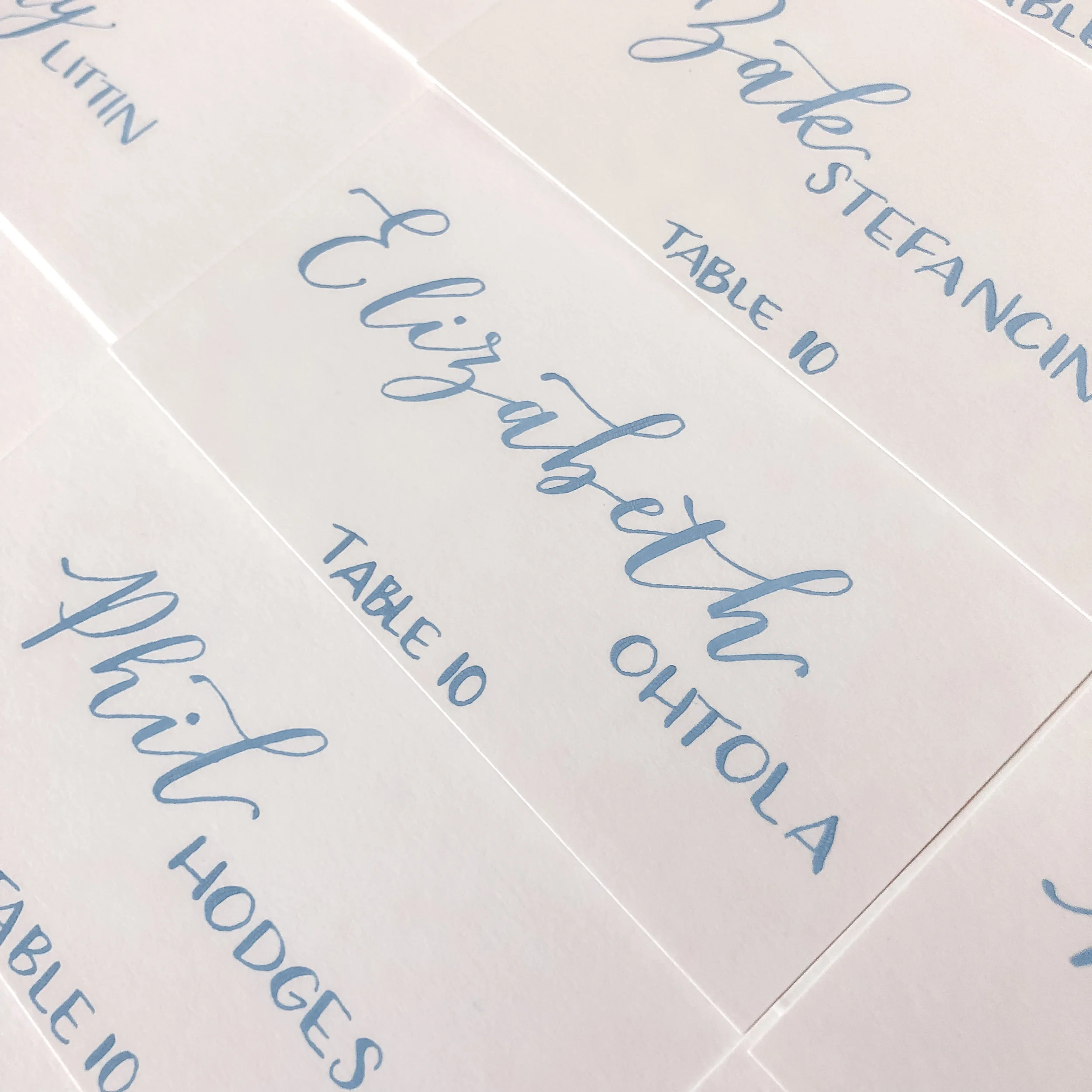 Close-up of dusty blue ink calligraphy escort cards on white paper.