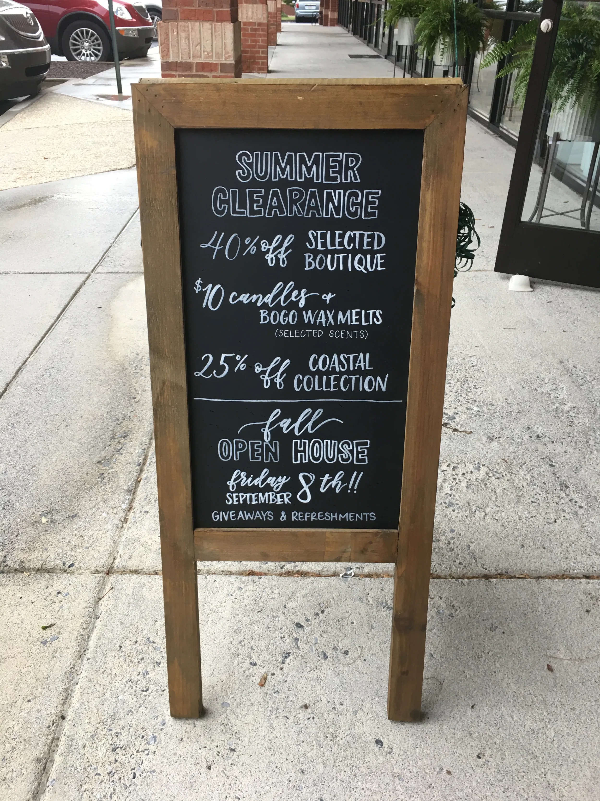 Wooden A-frame sidewalk chalkboard sign reading "Summer Clearance" outside a boutique shop.