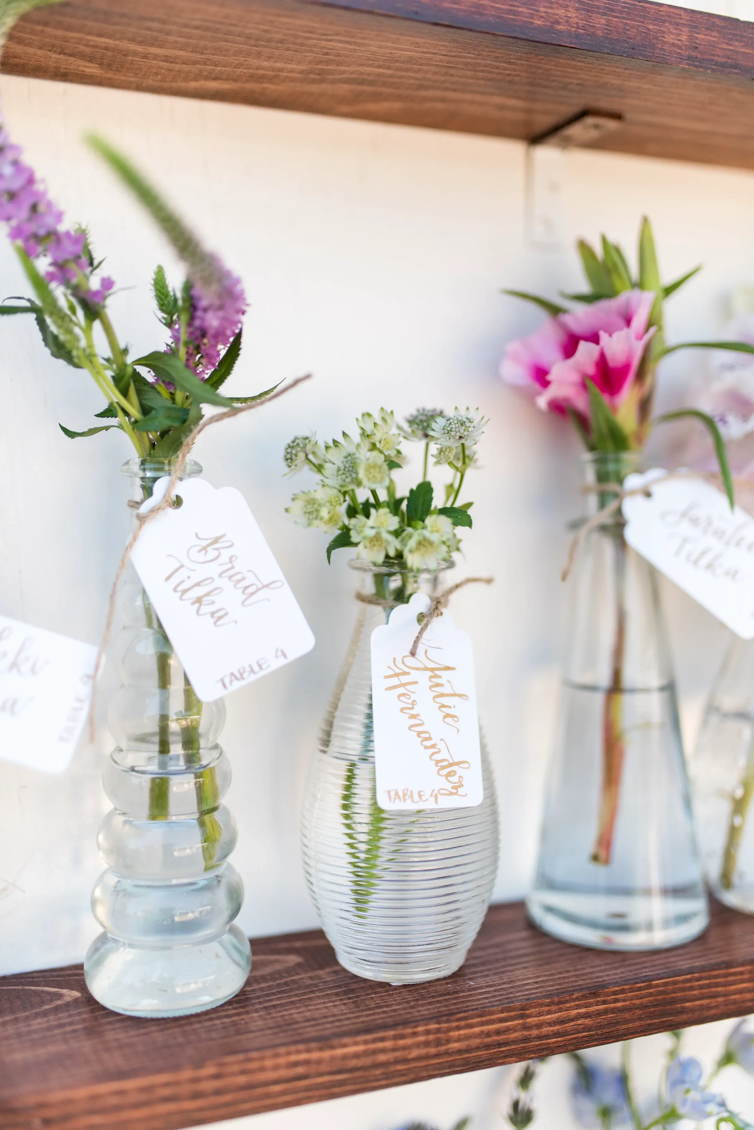 Custom hand-lettered wedding place card tags tied to floral bud vases at an outdoor Georgia venue.