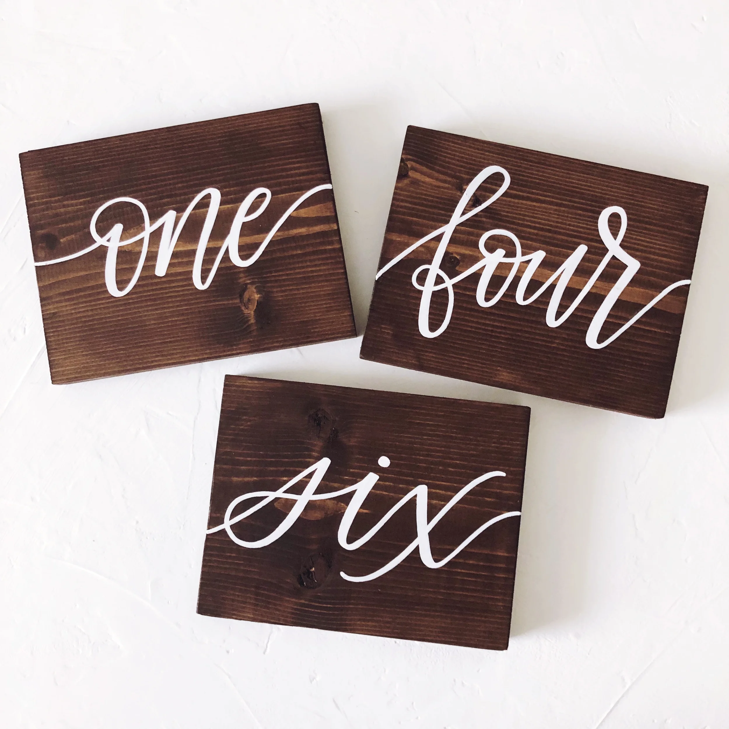 Rustic dark wood block table numbers with white cursive script.