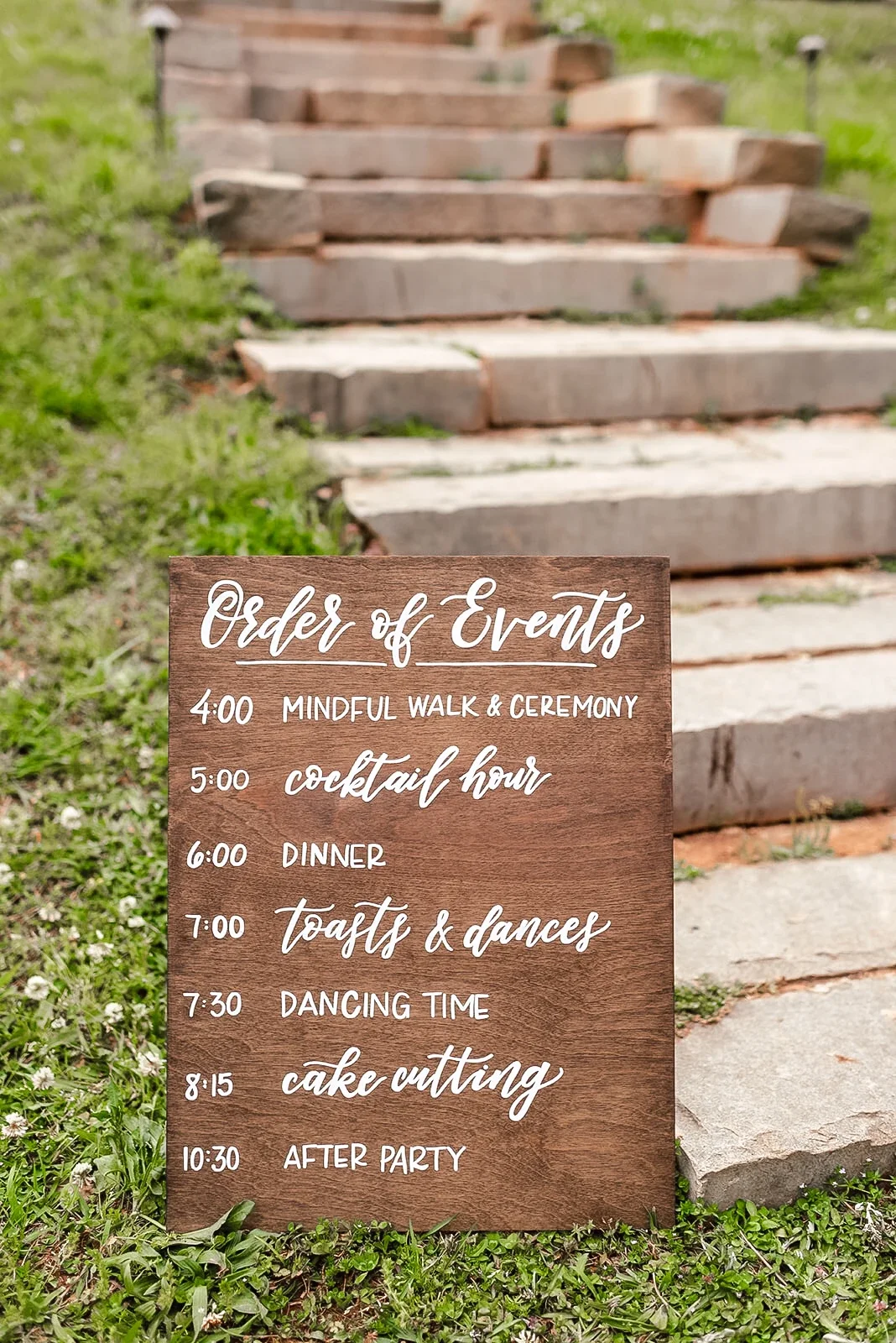 Stained wood "order of events" sign for wedding with times and events listed in white hand-lettering.