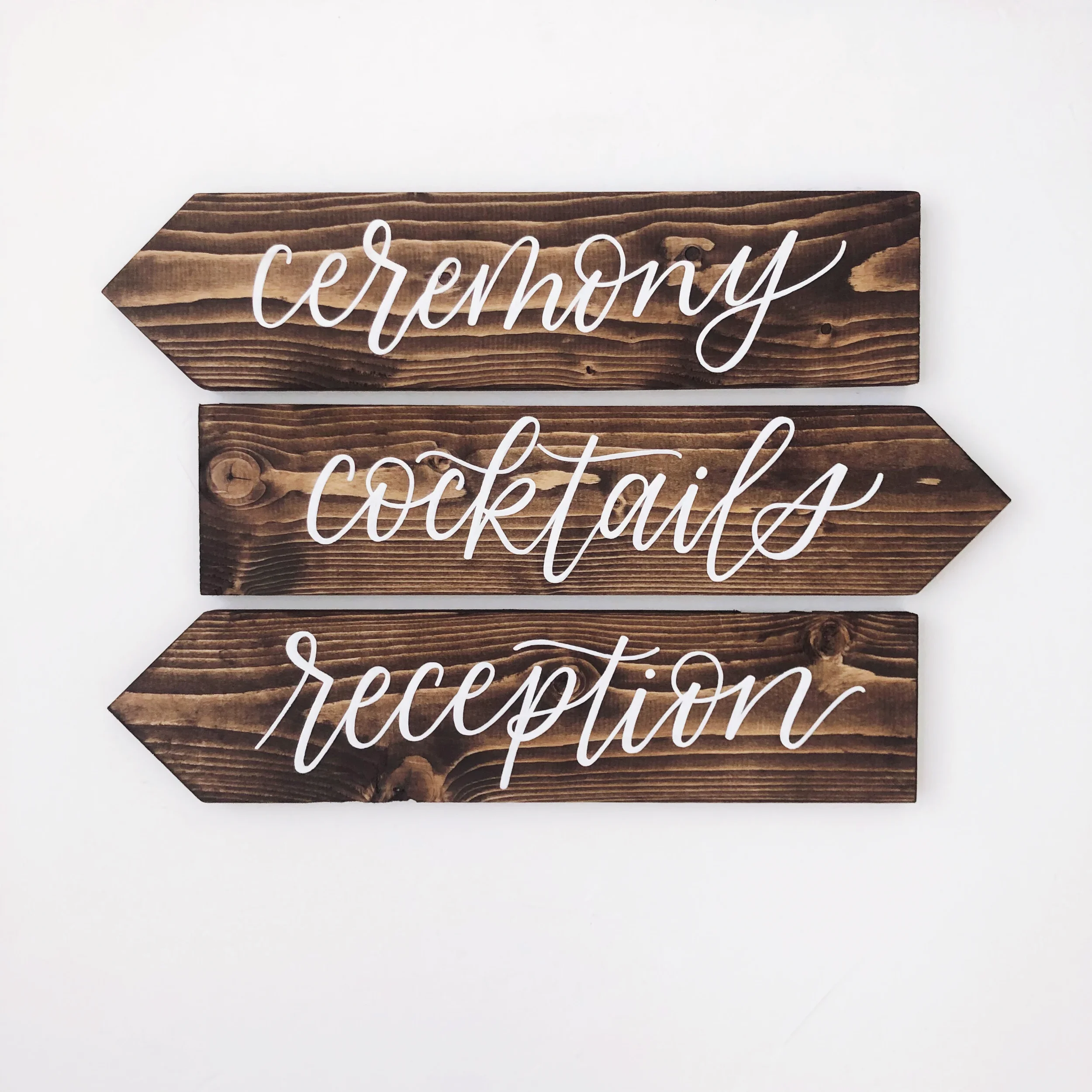 Outdoor wooden arrow signpost pointing guests toward the ceremony, reception, and cocktails.