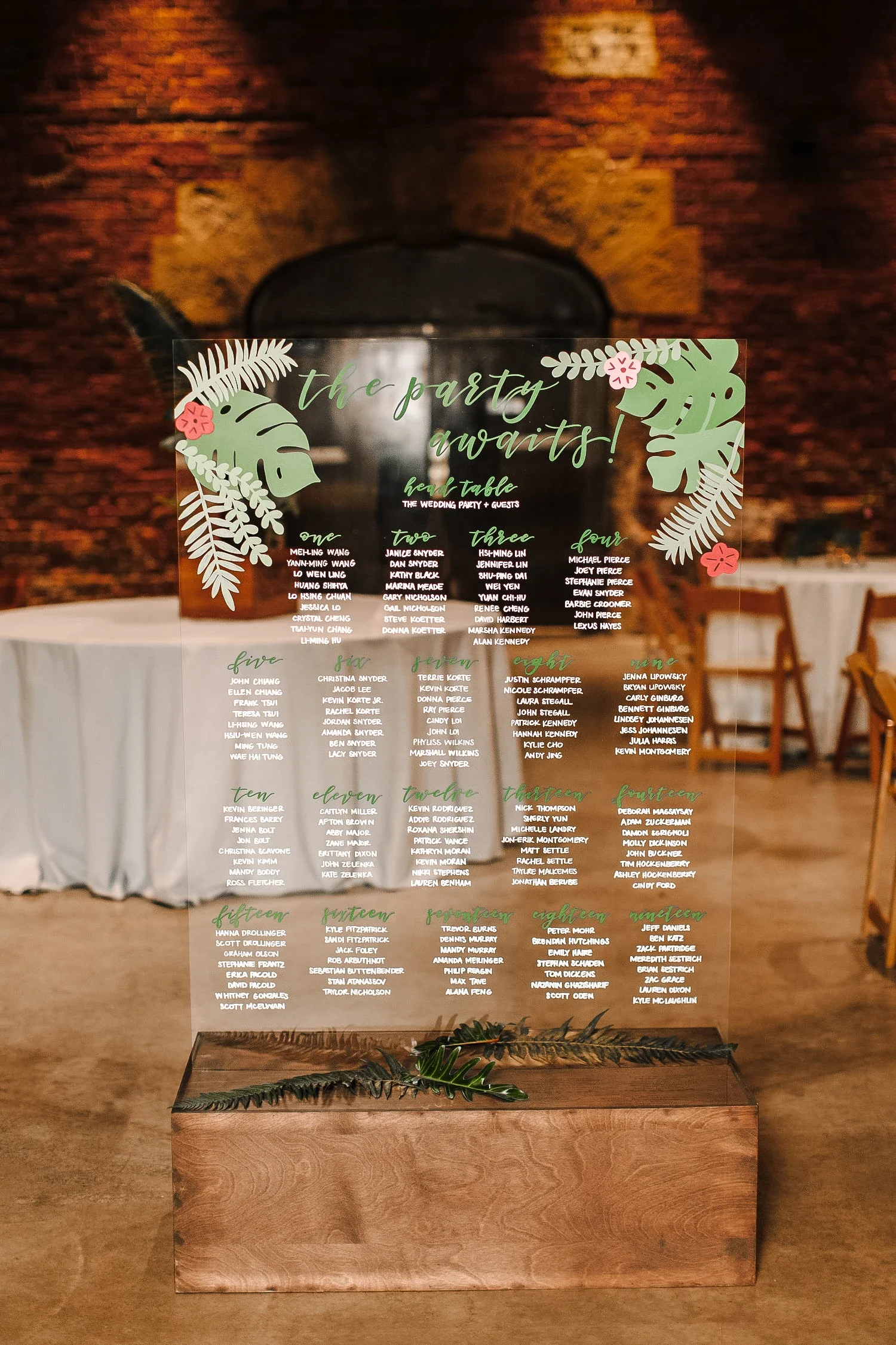 Move away from traditional paper seating walls with a large, freestanding clear acrylic wedding seating chart. Slotted into a custom dark wood base and styled with rich marsala florals, this striking transparent directory adds a modern, fine-art elem
