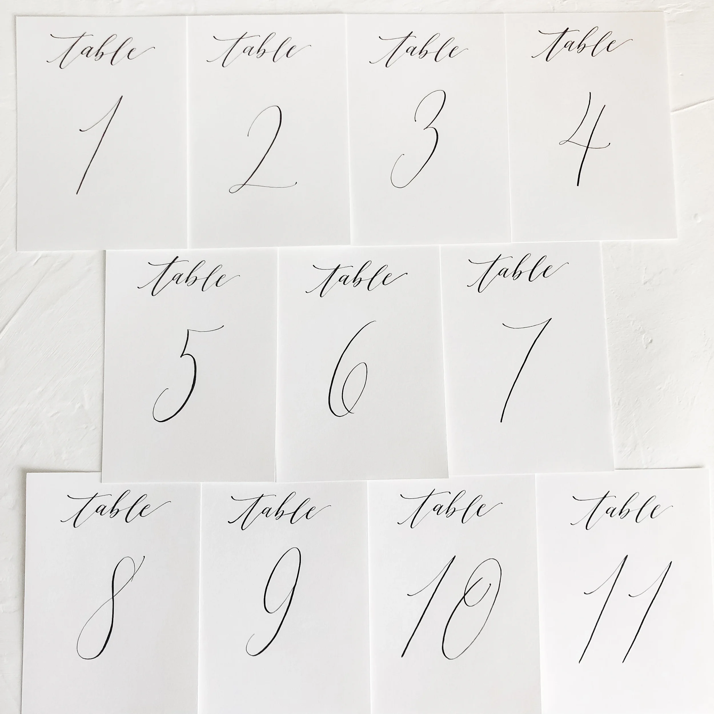Simple and classic white cardstock table numbers in black ink calligraphy.