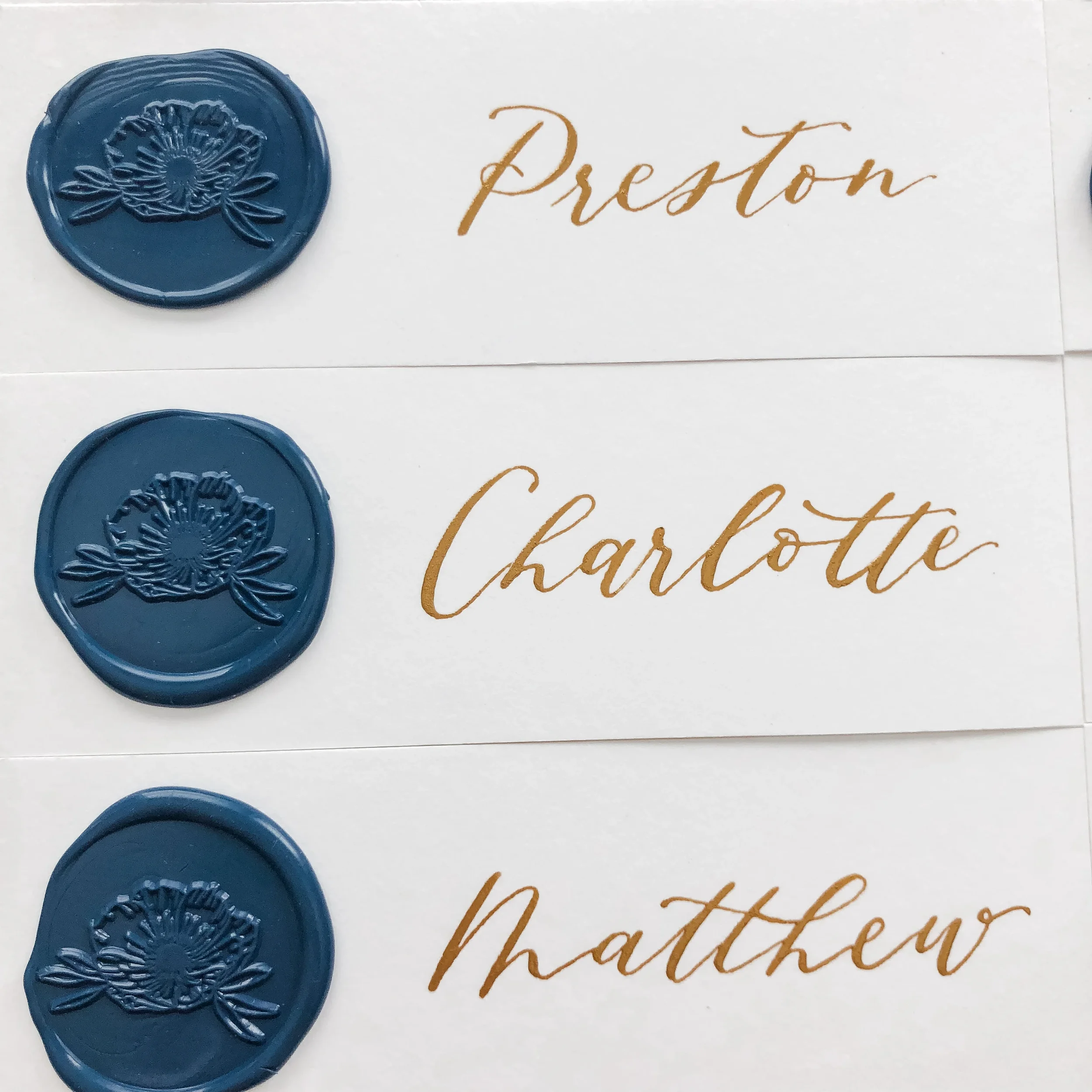 White paper escort ribbon strips with luxury gold calligraphy script and custom navy blue floral wax seals.