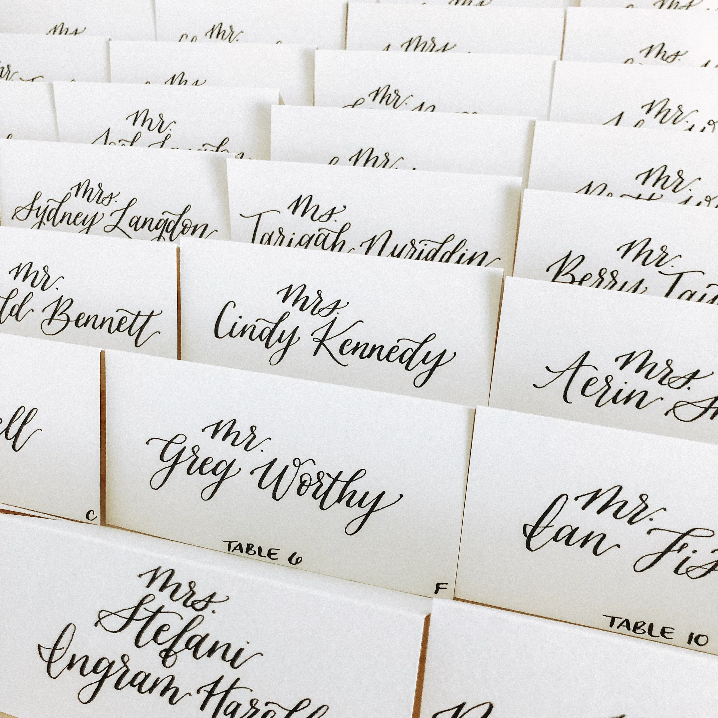 Minimalist white folded wedding place card with sharp black calligraphy script.