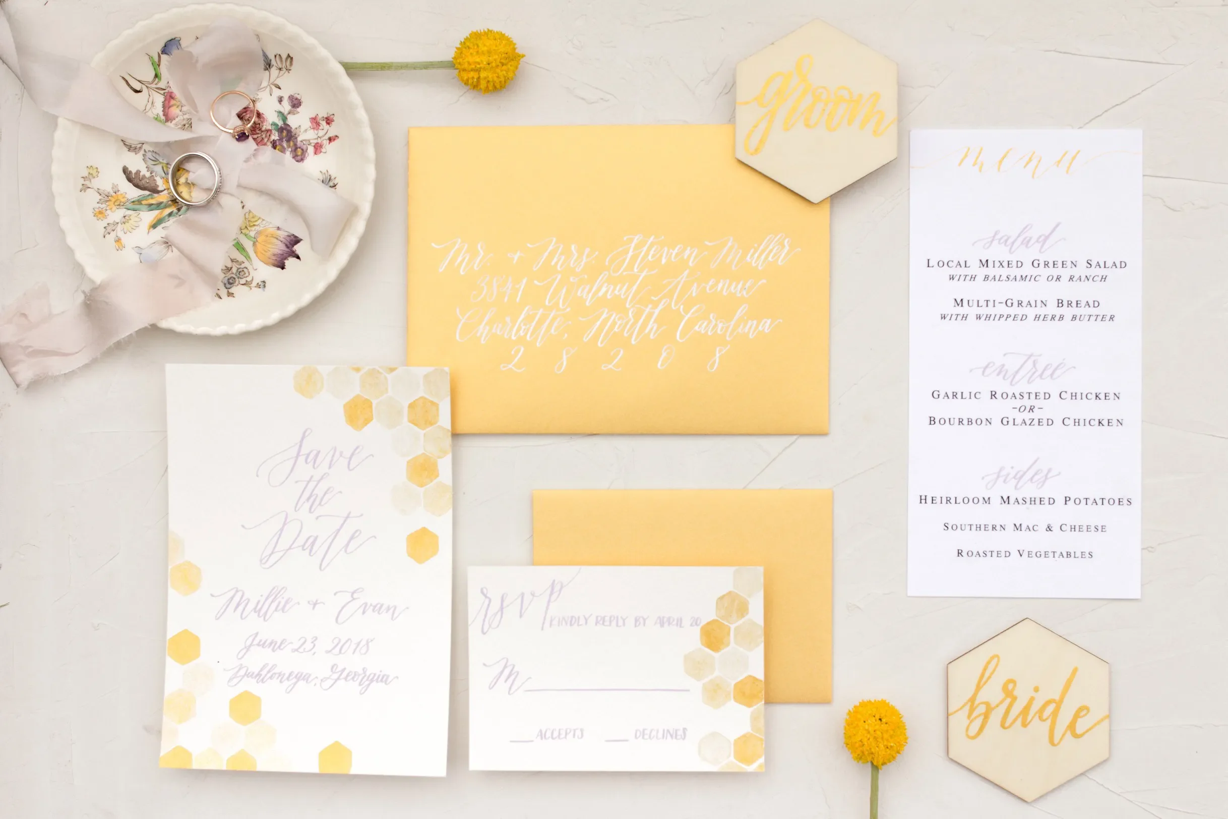 Bright yellow wedding invitation envelope with white calligraphy alongside a geometric honeycomb save the date.