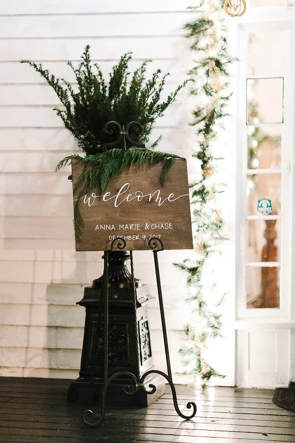 Simple wedding welcome wood sign written in white ink script on a black scroll easel.