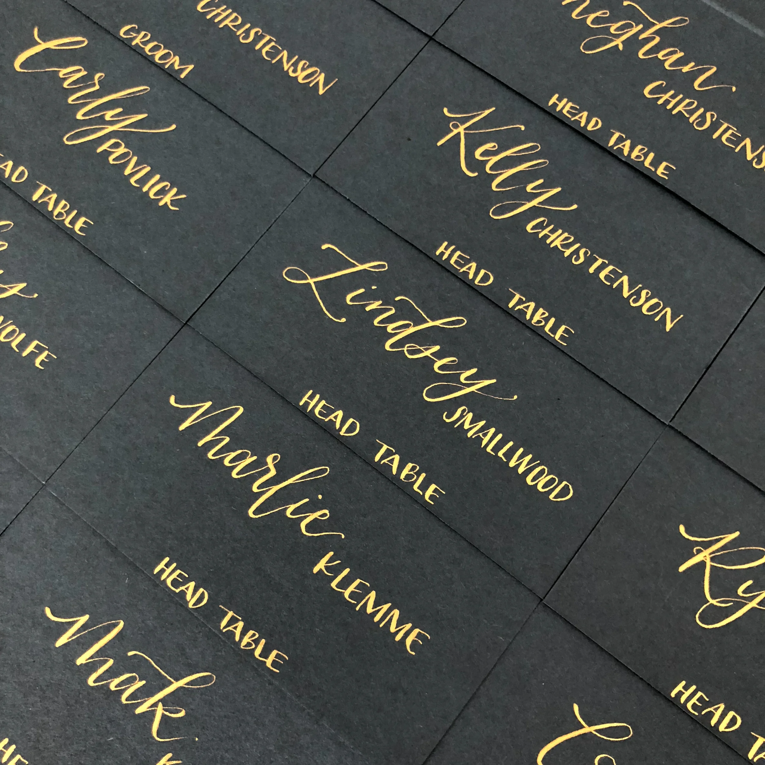 Array of matte black escort cards featuring elegant metallic gold calligraphy script for head table seating.