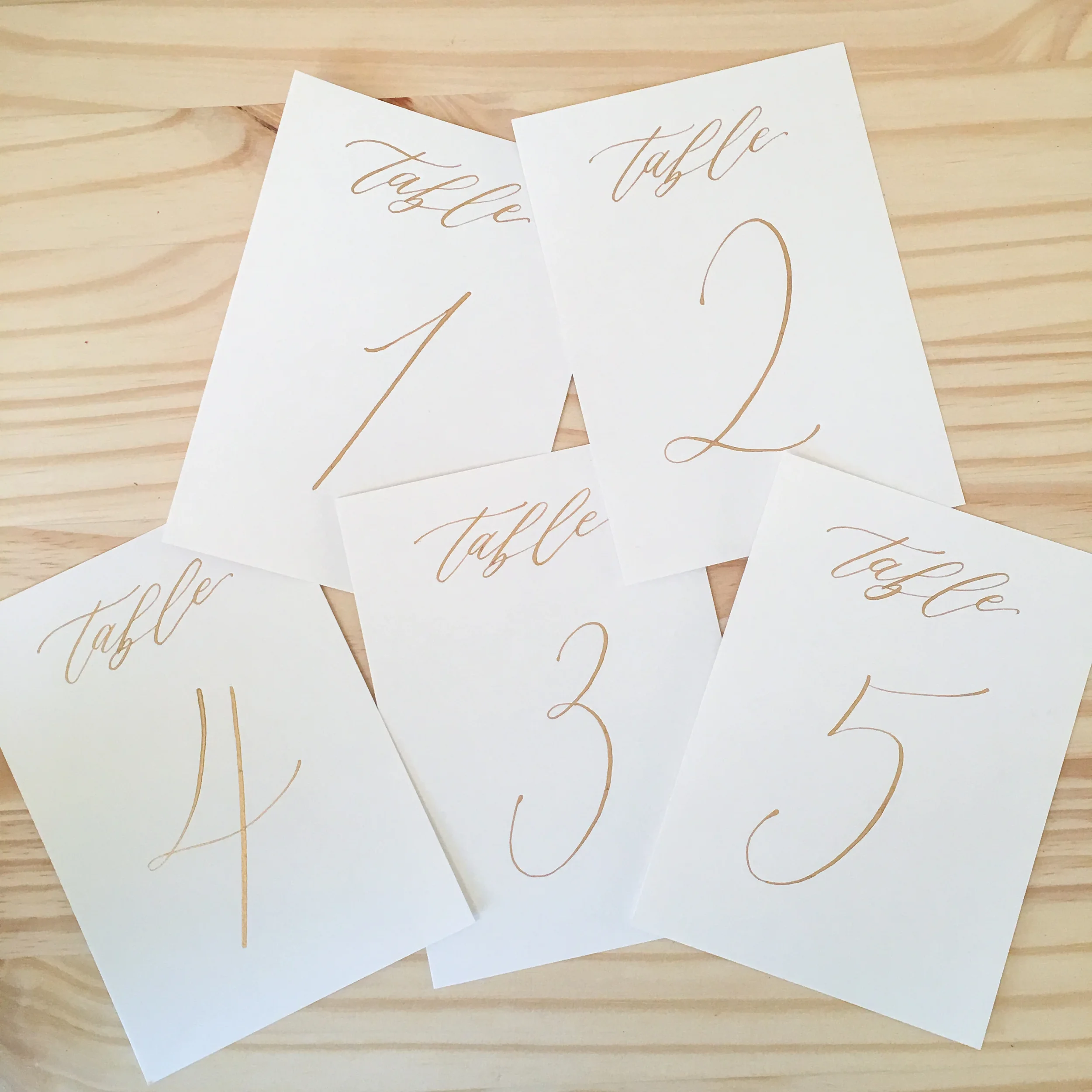 Elegant calligraphed wedding table numbers printed on clean white paper and gold ink calligraphy ink.