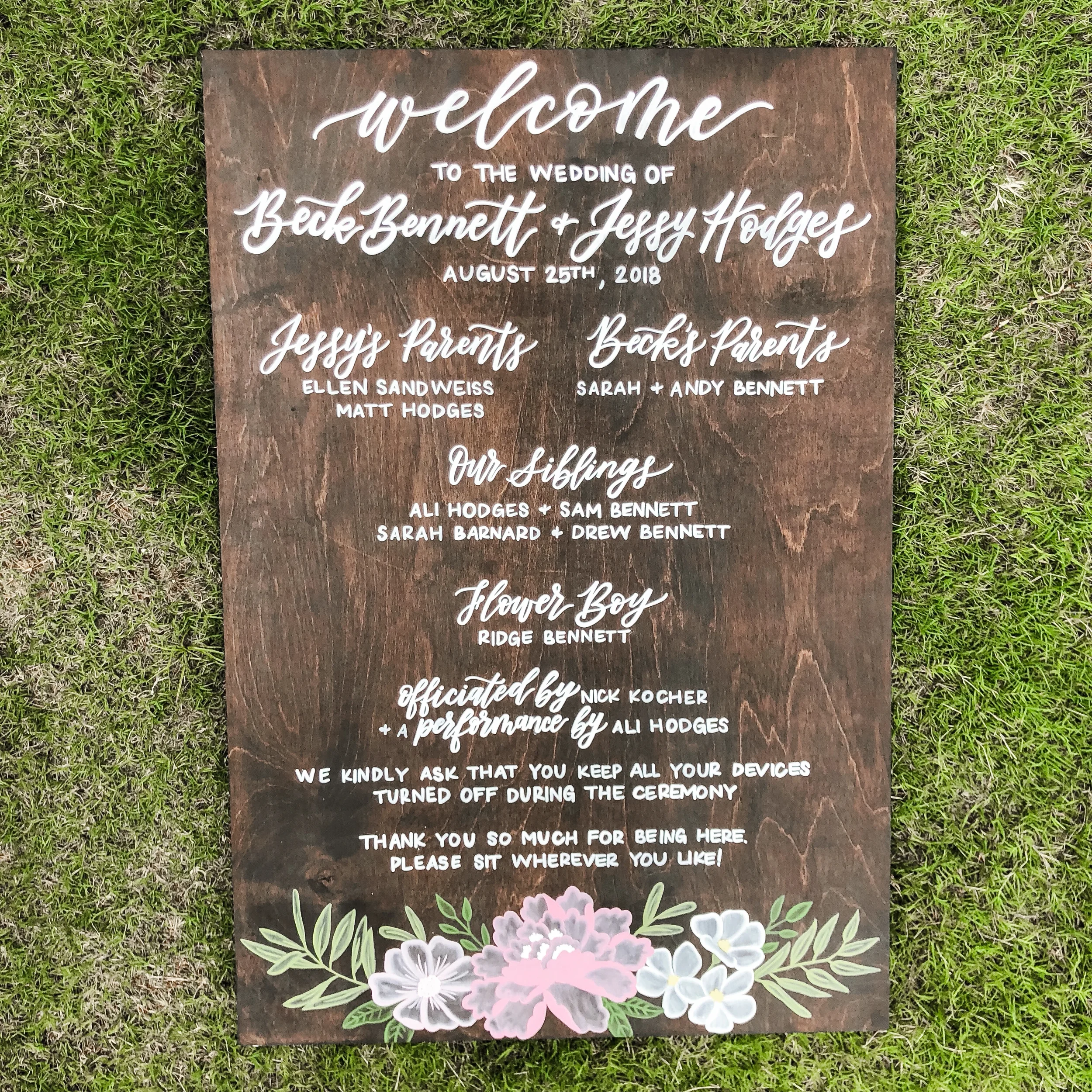 Replace traditional paper programs with a large, eco-friendly wooden wedding program board. Detailed with sweeping white calligraphy, painted floral illustrations, and full wedding party listings, this stained wood sign keeps guests informed while se