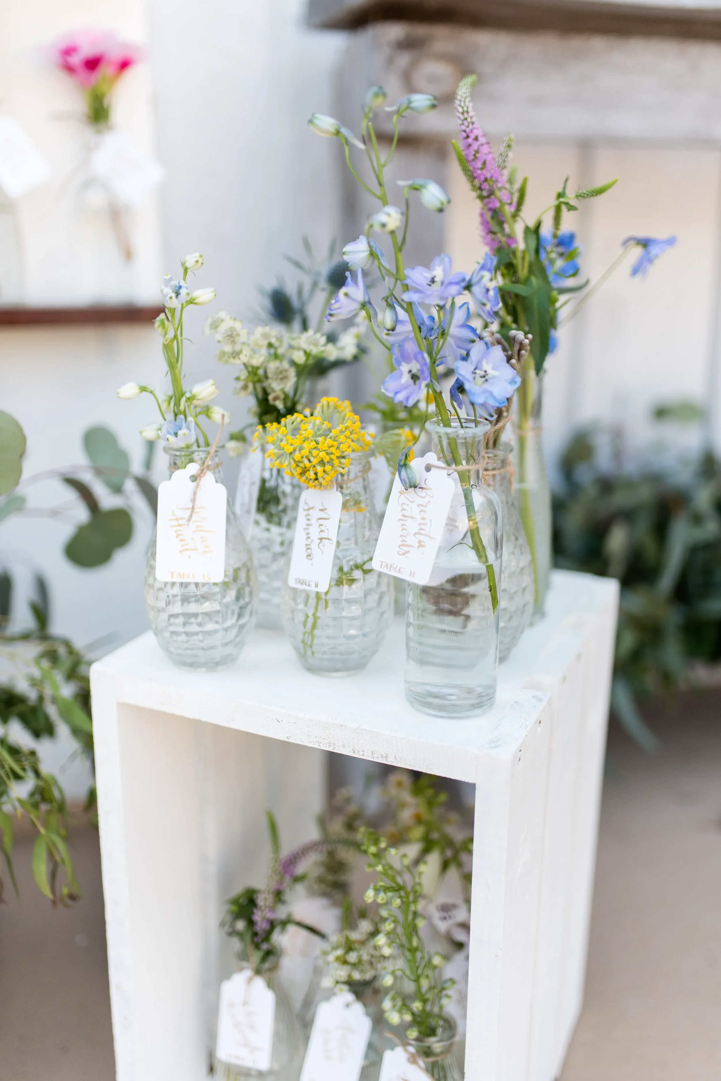 Bring a whimsical, fine-art feel to your Georgia countryside reception with an interactive floral seating chart. Our hand-lettered escort tags add a personalized, luxurious touch to rustic wooden shelving and mismatched clear glass vases.