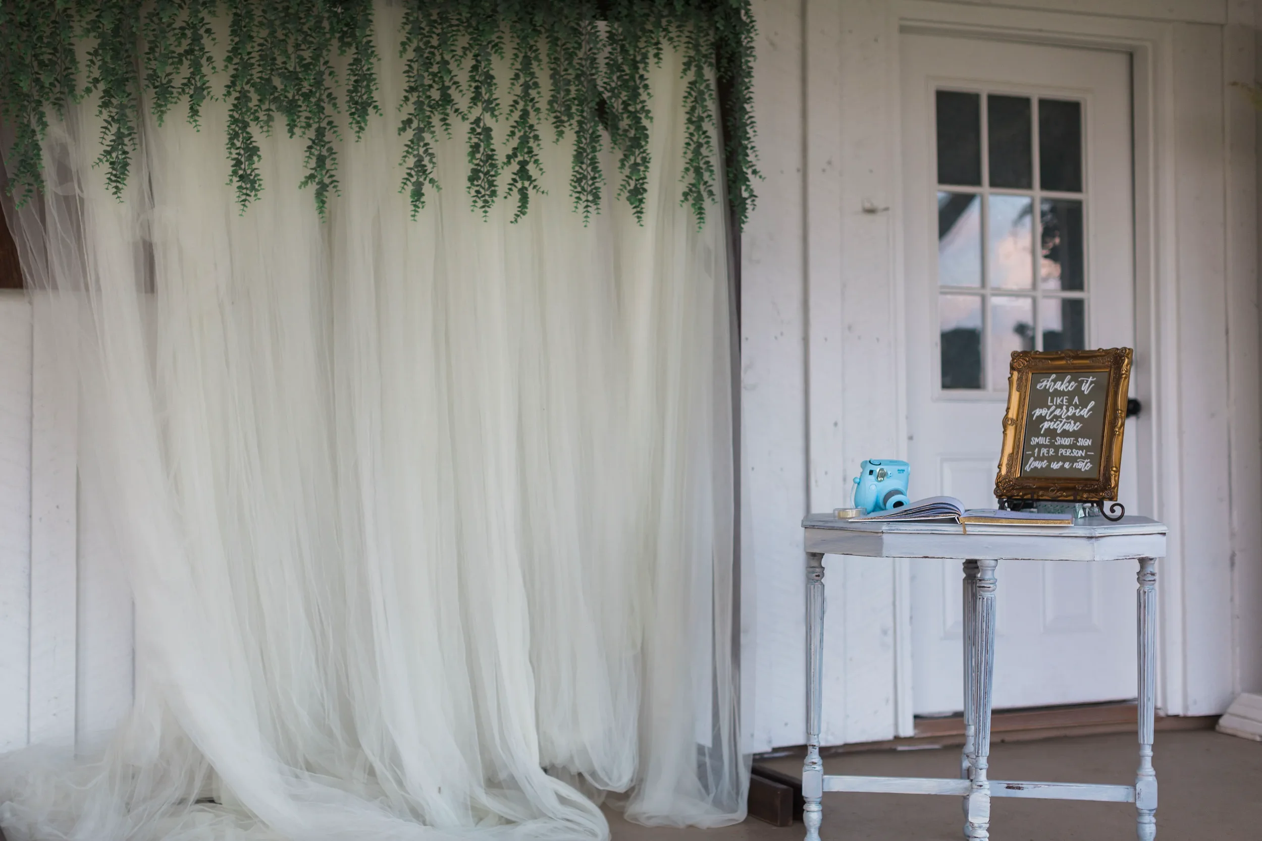 Encourage your guests to capture the moment with an interactive instant photo guestbook station. Fronted by a charming vintage gold mirror sign with custom script calligraphy, this playful setup pairs a pastel Instax camera with a personalized scrapb