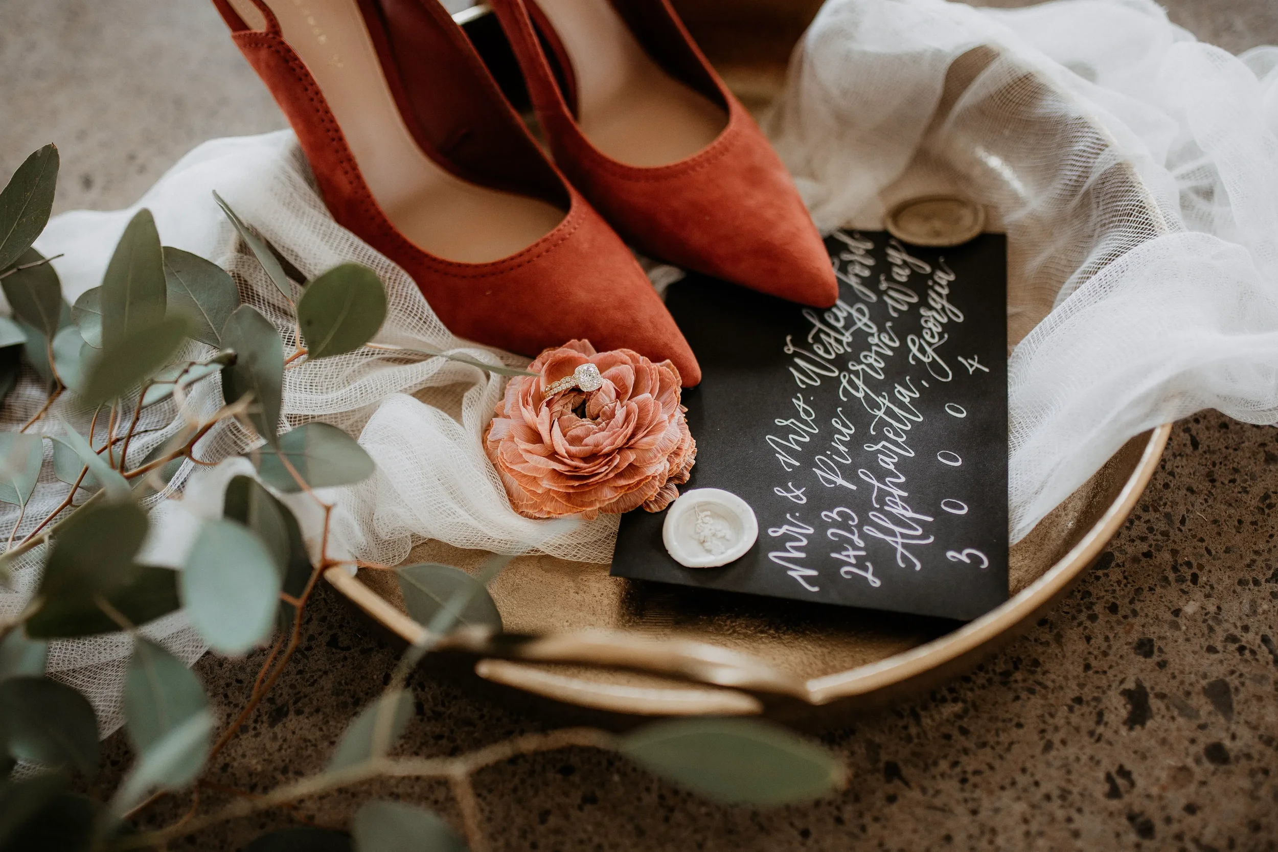 High-contrast wedding details flat lay with white ink script on black paper and fresh eucalyptus greenery.