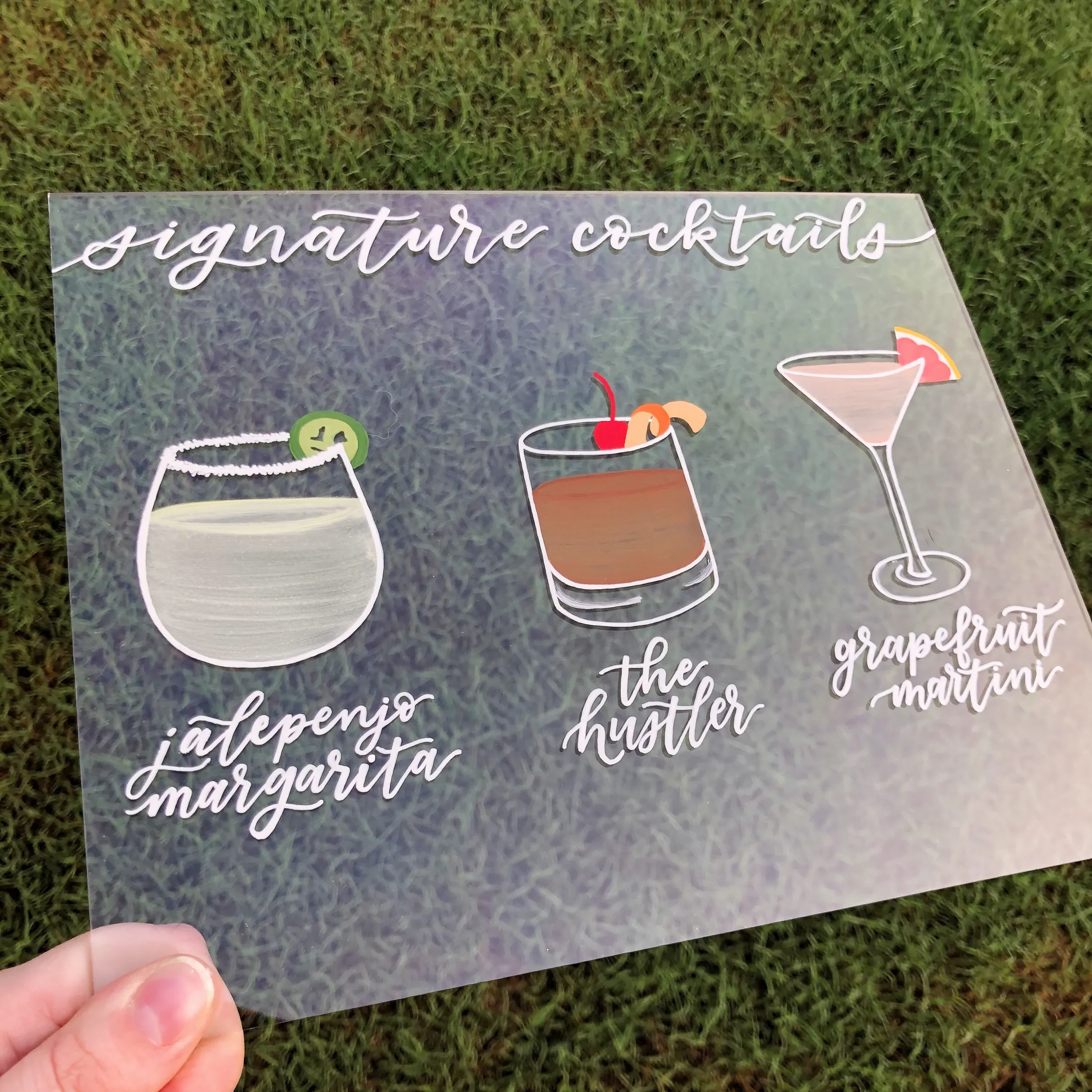 Clear acrylic signature cocktails wedding sign featuring detailed hand-painted drink illustrations.