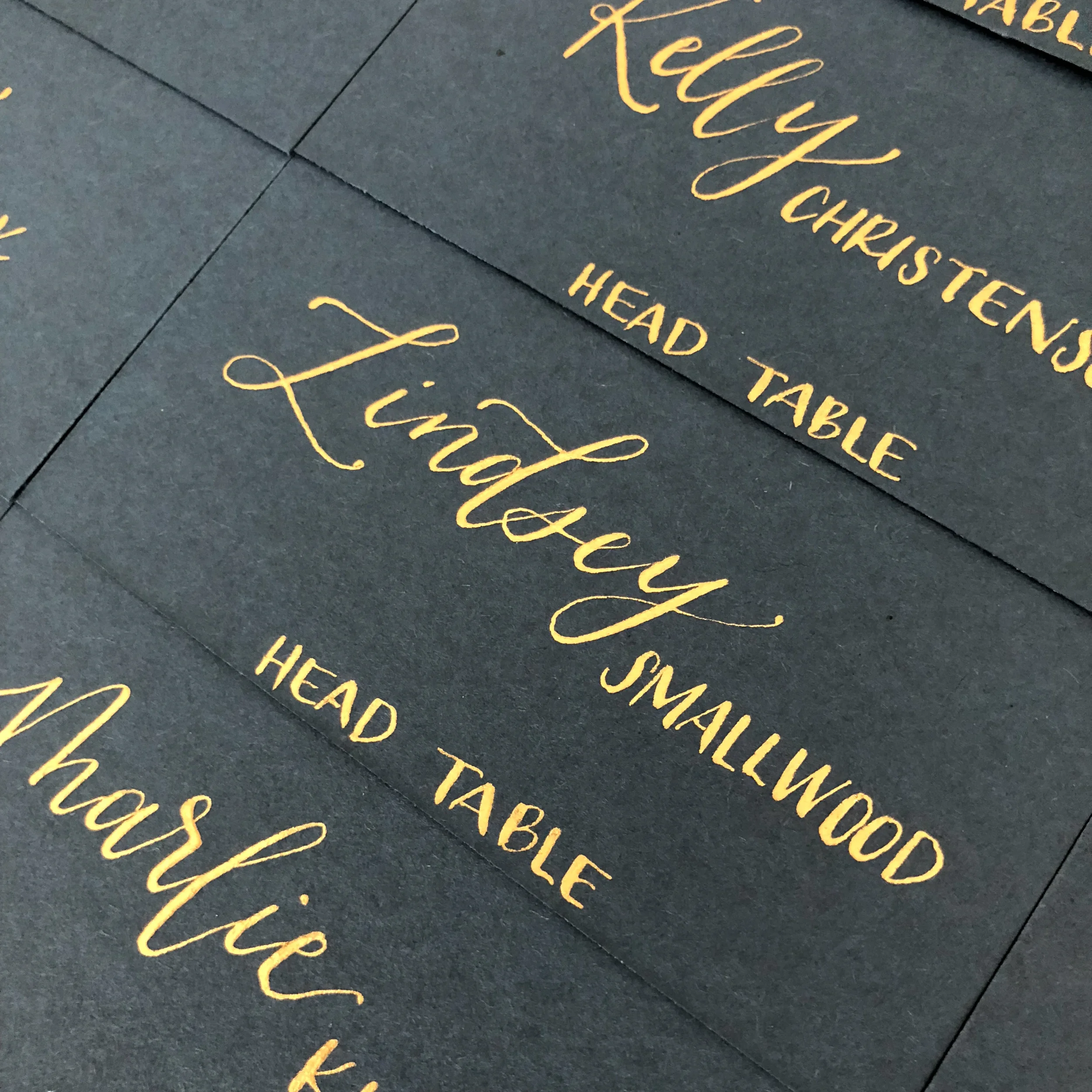 High-contrast modern wedding place cards with gold hand-lettered names.