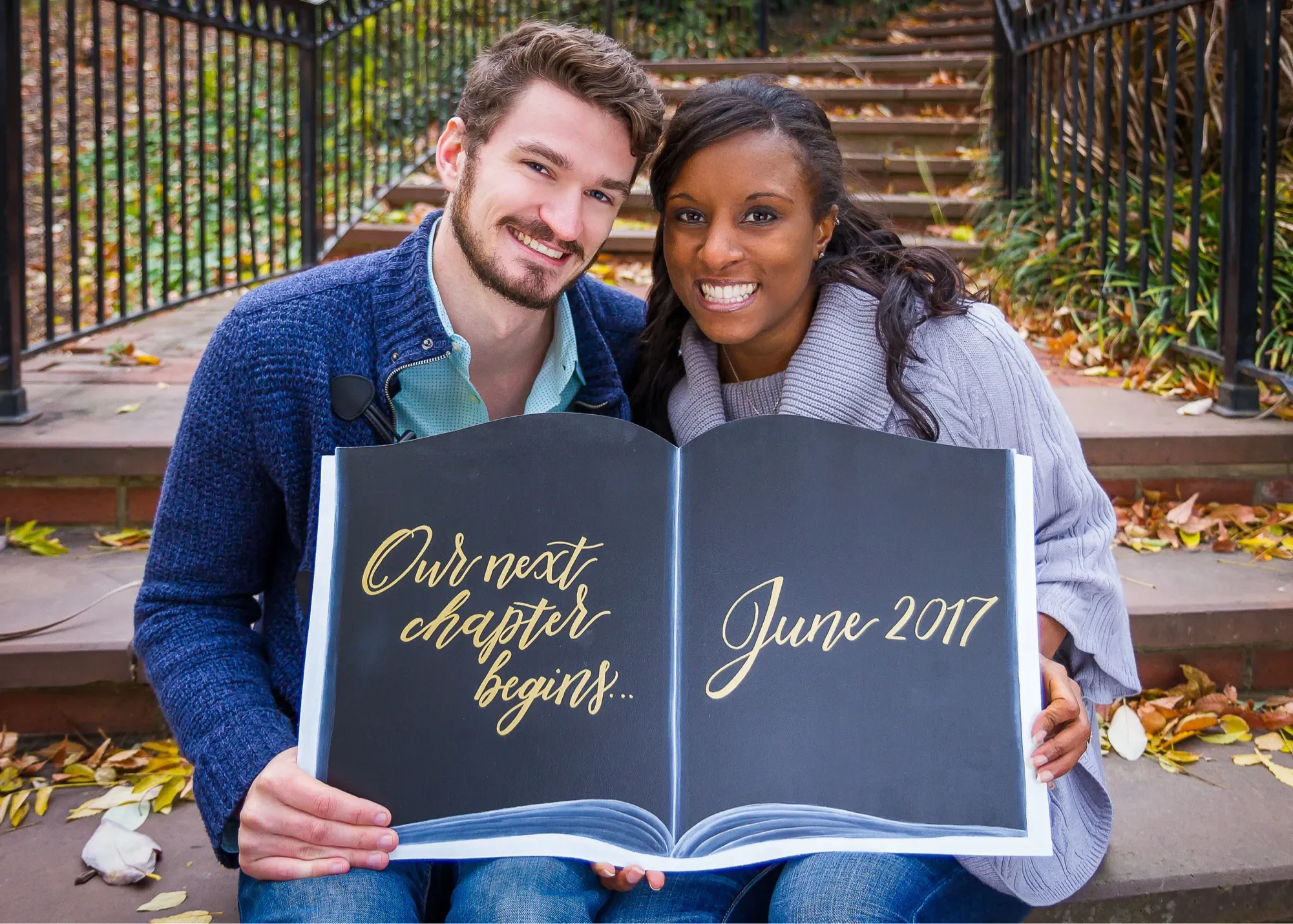 Tell your love story with a unique, interactive engagement photoshoot prop. This custom open-book shaped chalkboard sign reads "Our next chapter begins..." alongside the couple's wedding date in elegant gold and white hand-lettering, creating a whims