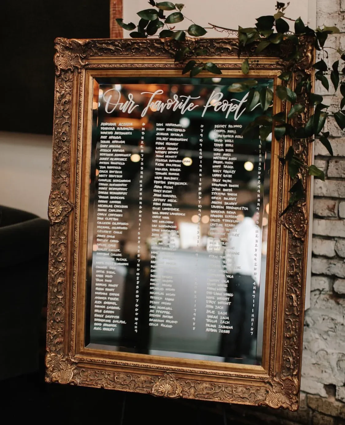 Make finding seats an luxurious experience with a large vintage gold mirror seating chart. Hand-lettered with "Our Favorite People" across the top and organized guest table assignments below, this framed glass sign adds timeless elegance and venue re