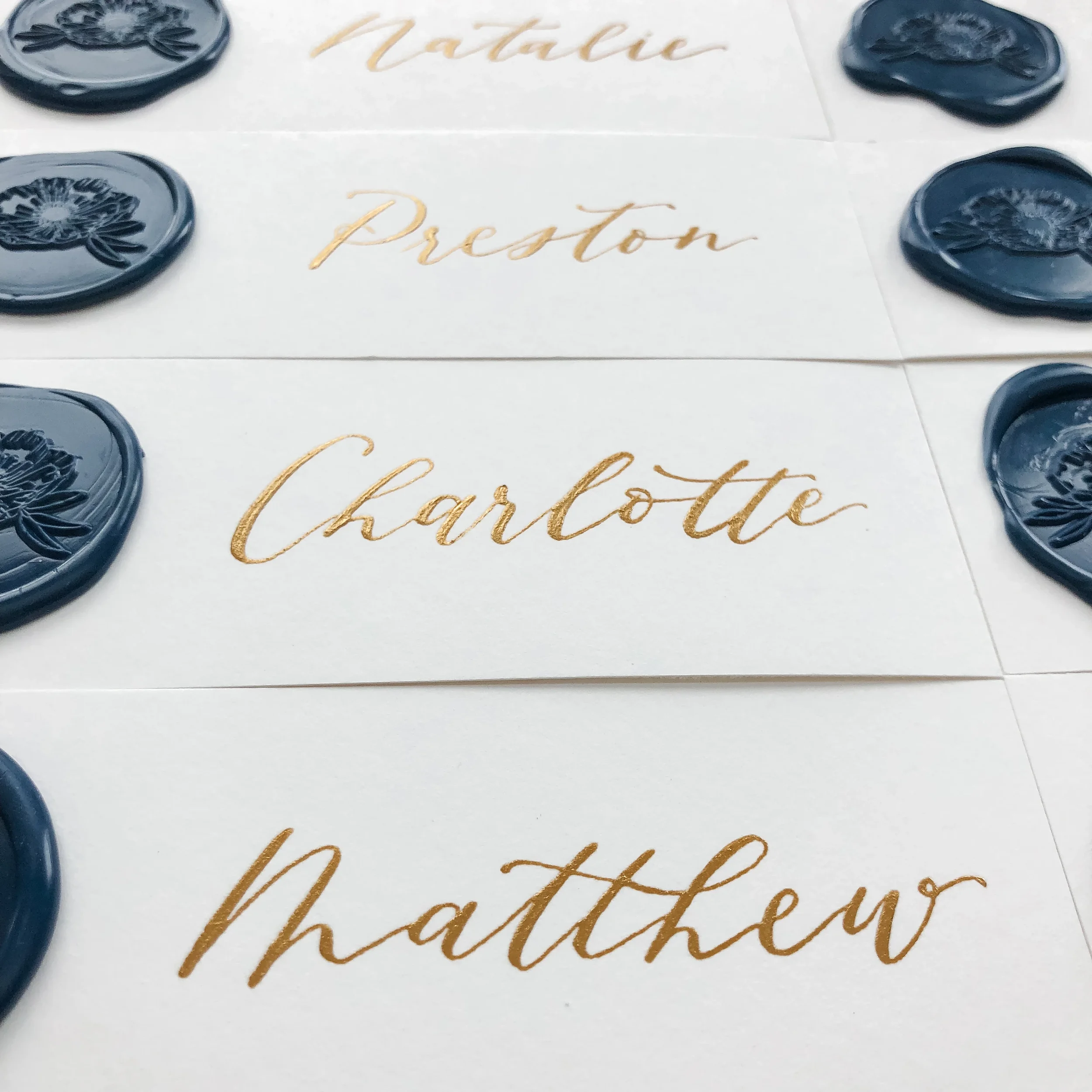 Fine-art wedding place cards adorned with metallic gold hand-lettering and detailed blue wax stamps.