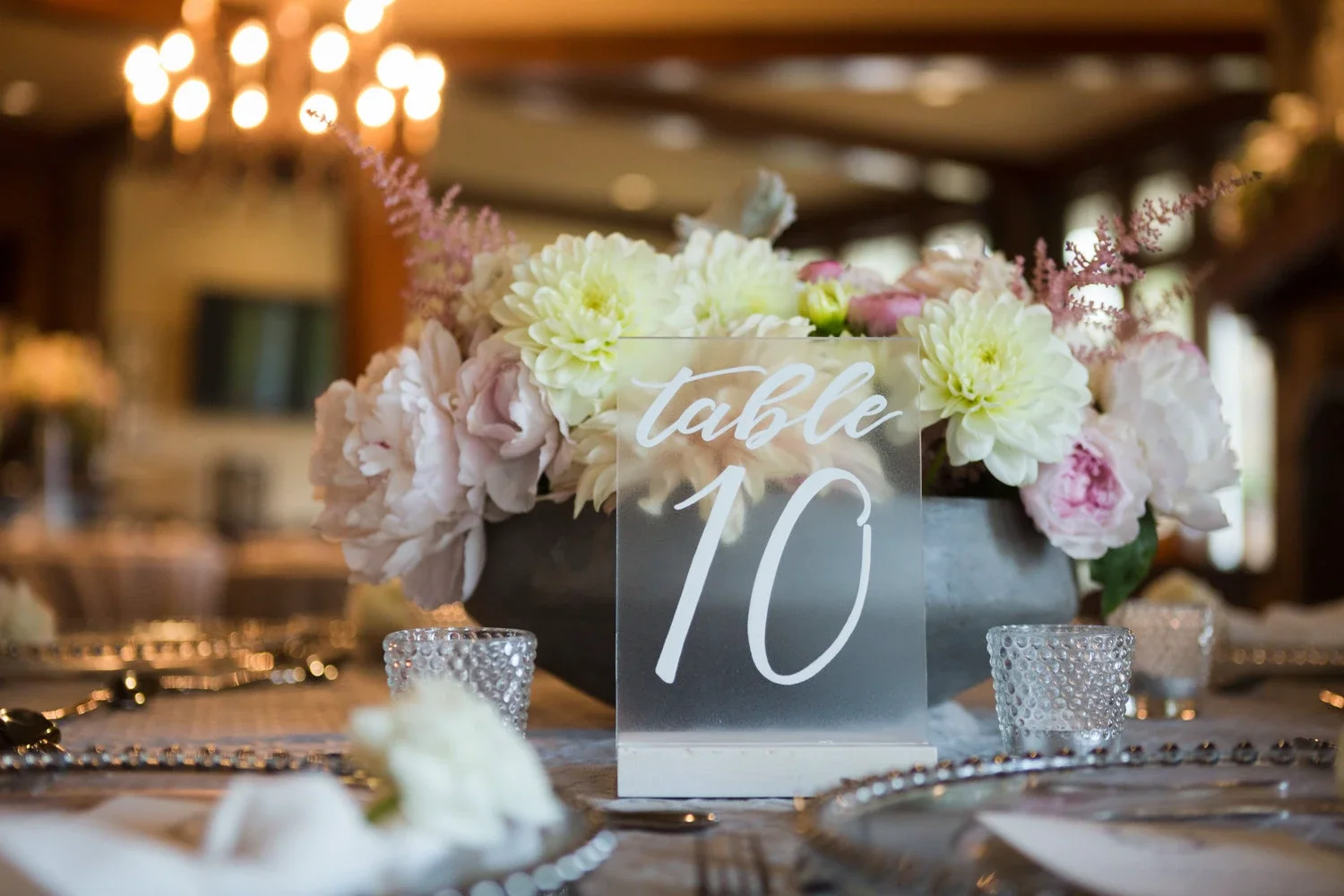 Modern clear acrylic table number with white calligraphy script set in a natural wooden stand.