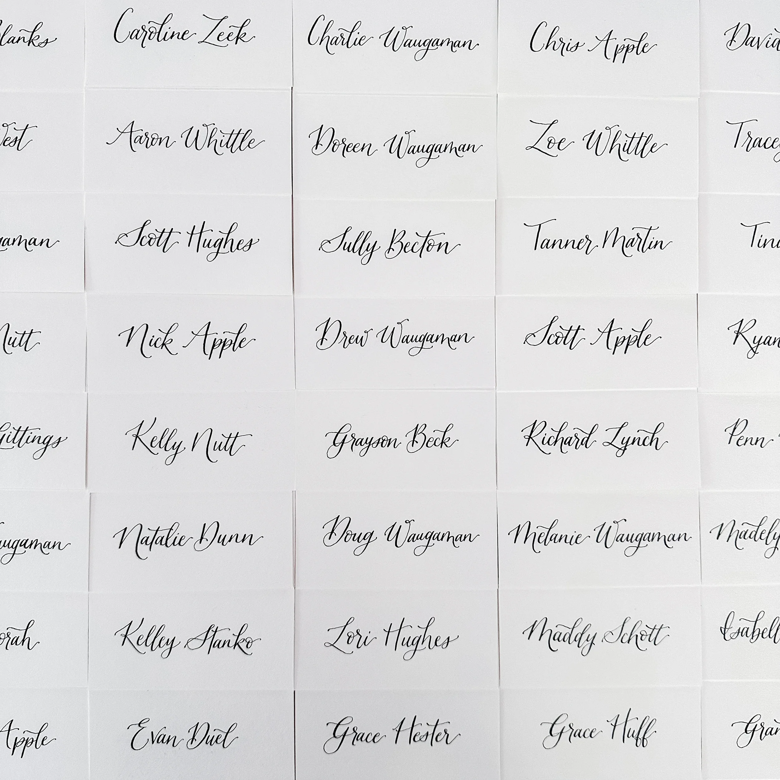 Embrace the timeless elegance of minimalist day-of stationery with a classic white folded place card. Showcasing clean, high-contrast black script calligraphy, this simple paper name card rests beautifully on natural wood or formal linen settings for