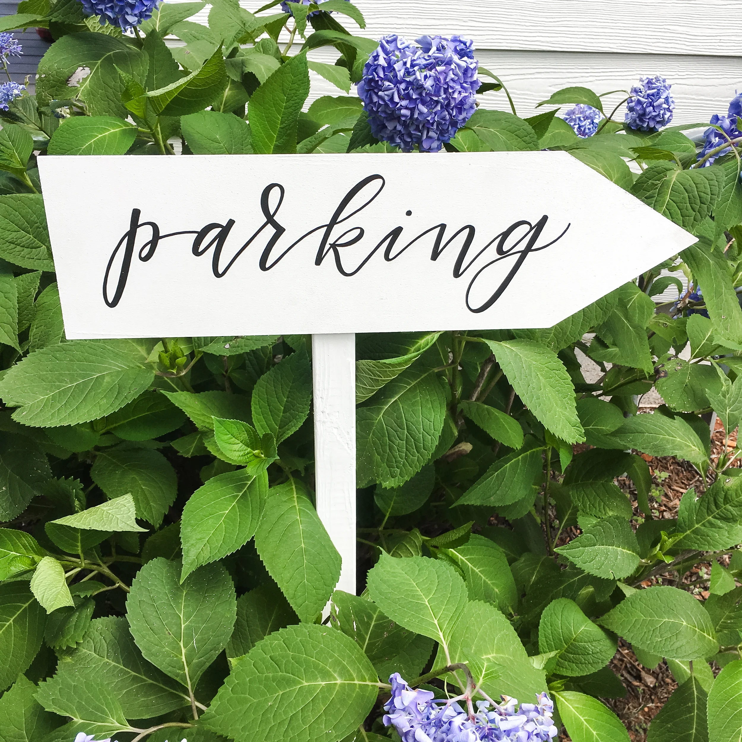 Outdoor white wooden arrow signpost pointing guests toward parking lot at a wedding venue.