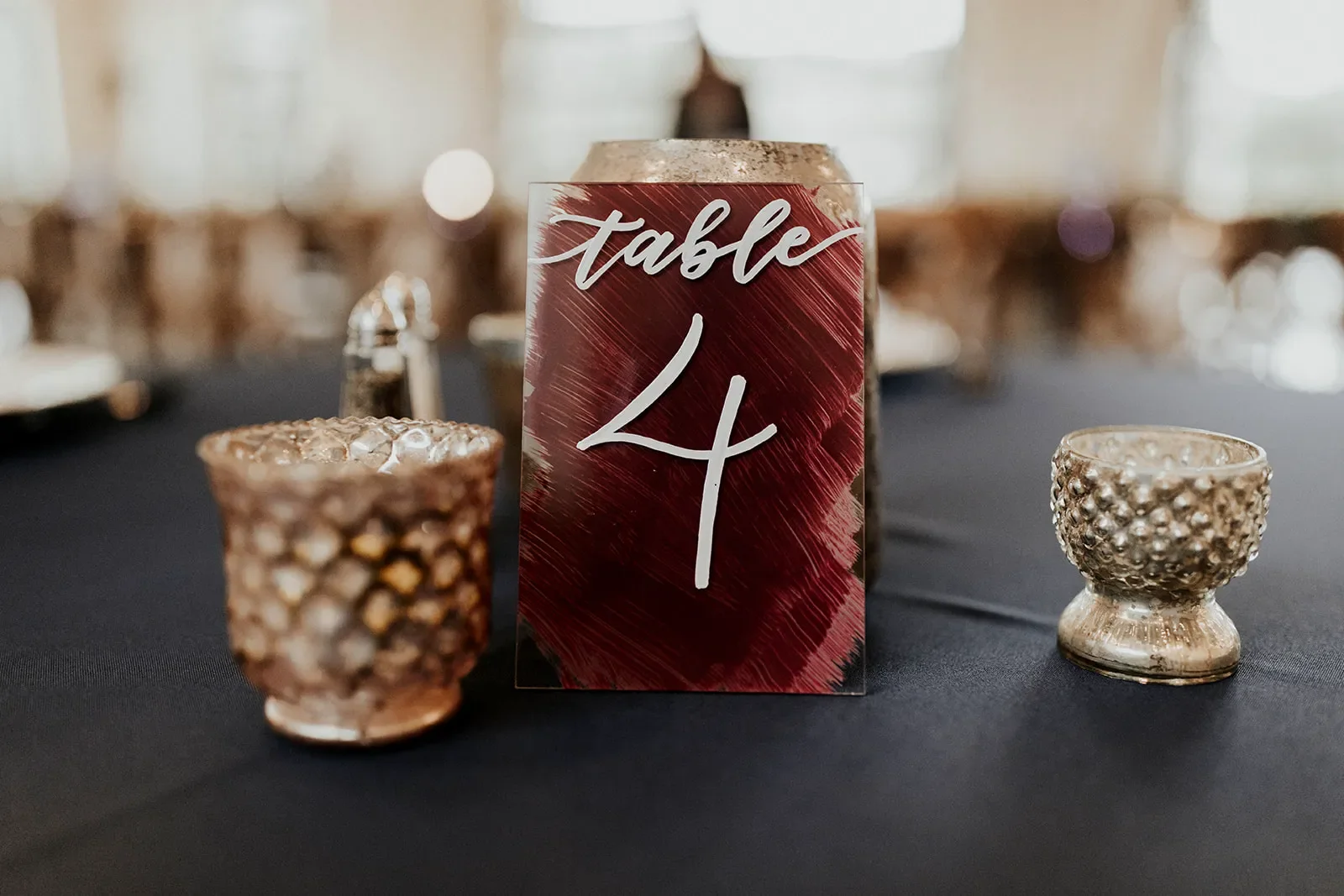 Close-up of acrylic table number 4 with a textured burgundy painted back and white script font.
