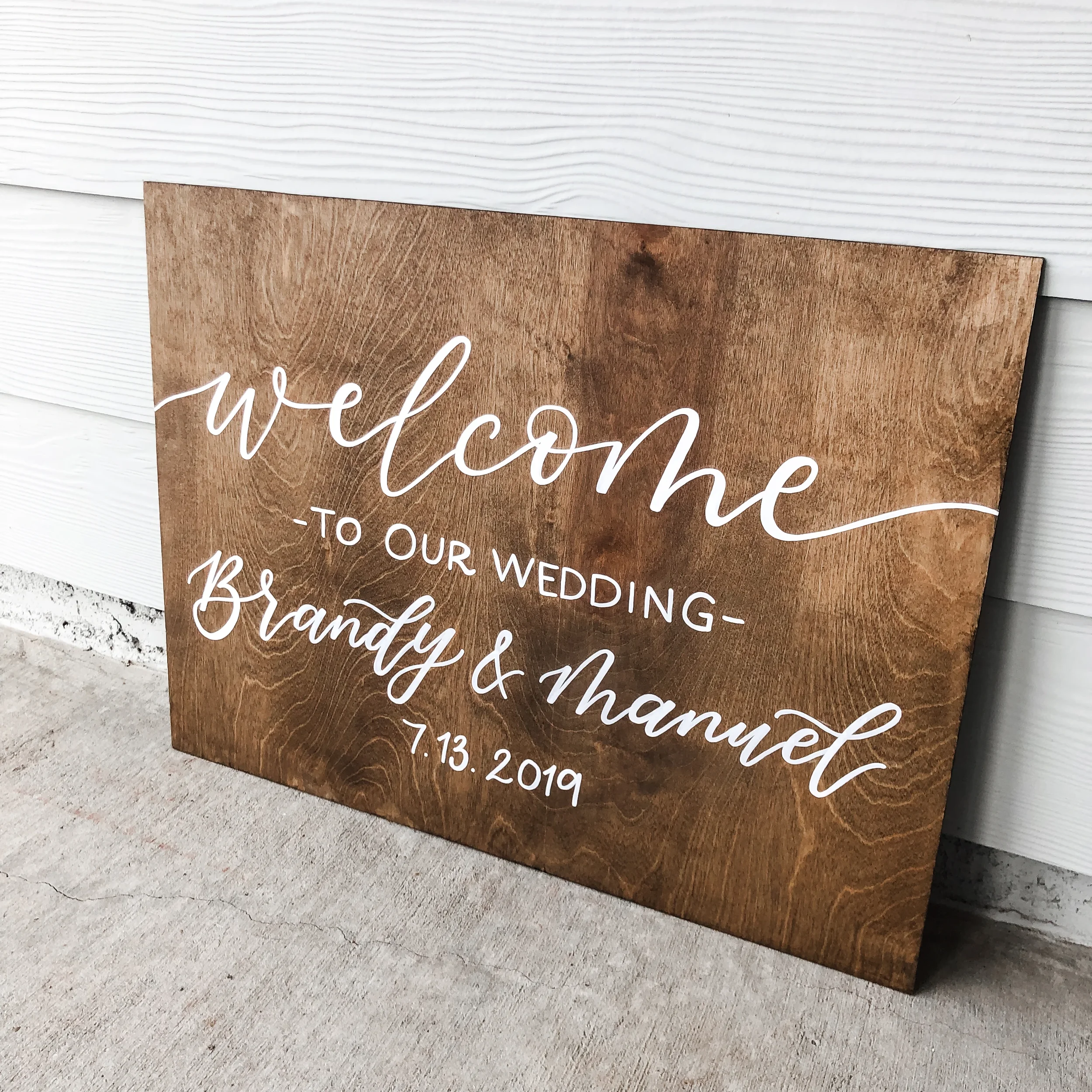 Rustic wooden wedding welcome board featuring modern calligraphy script and event date displayed outdoors.