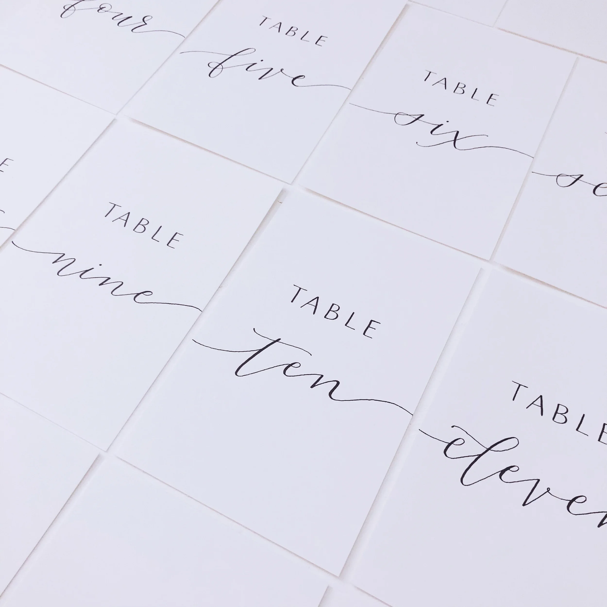 Minimalist paper wedding table numbers written in delicate black calligraphy script and block lettering.