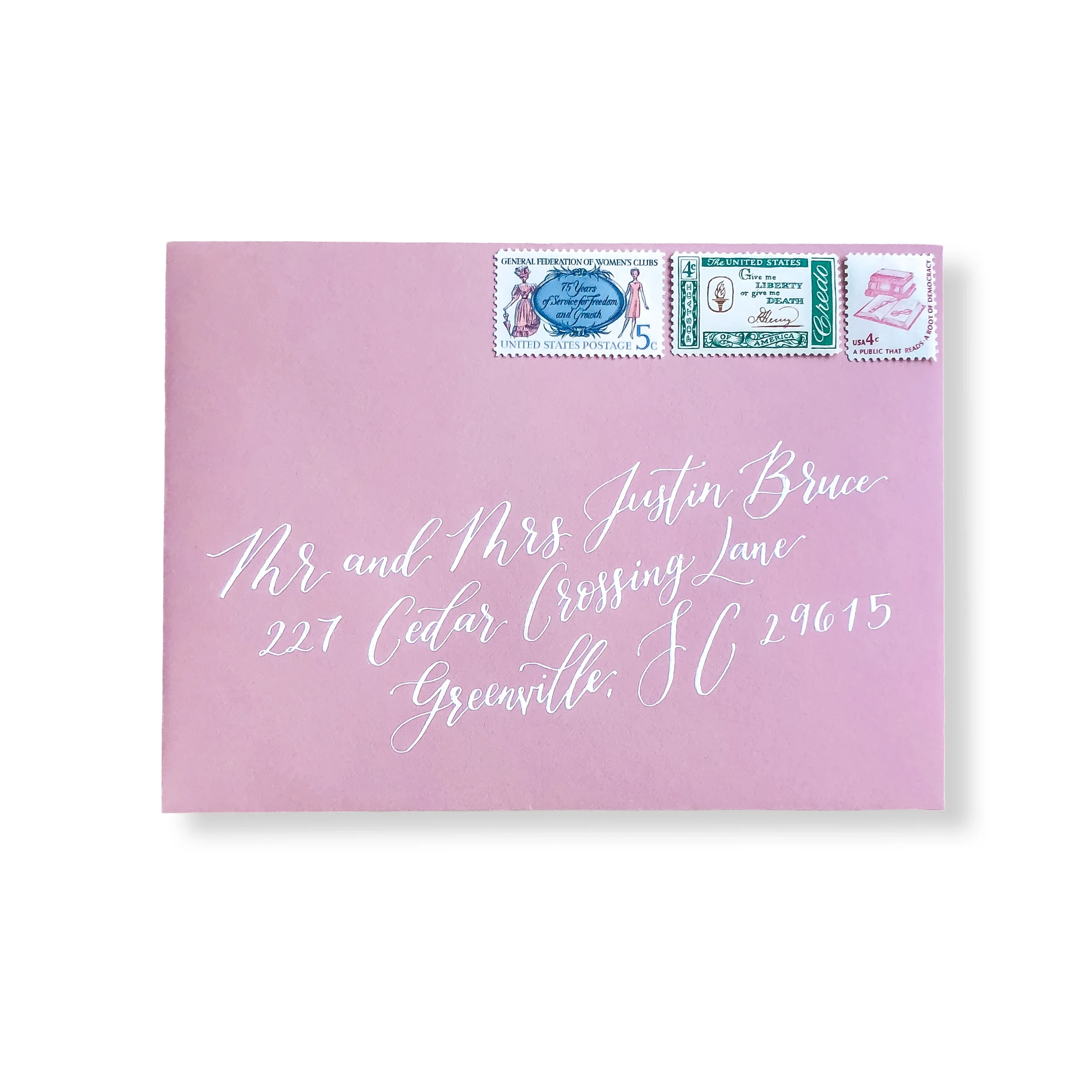 Blush pink wedding guest envelope with white in calligraphy and an assortment of matching vintage stamps.
