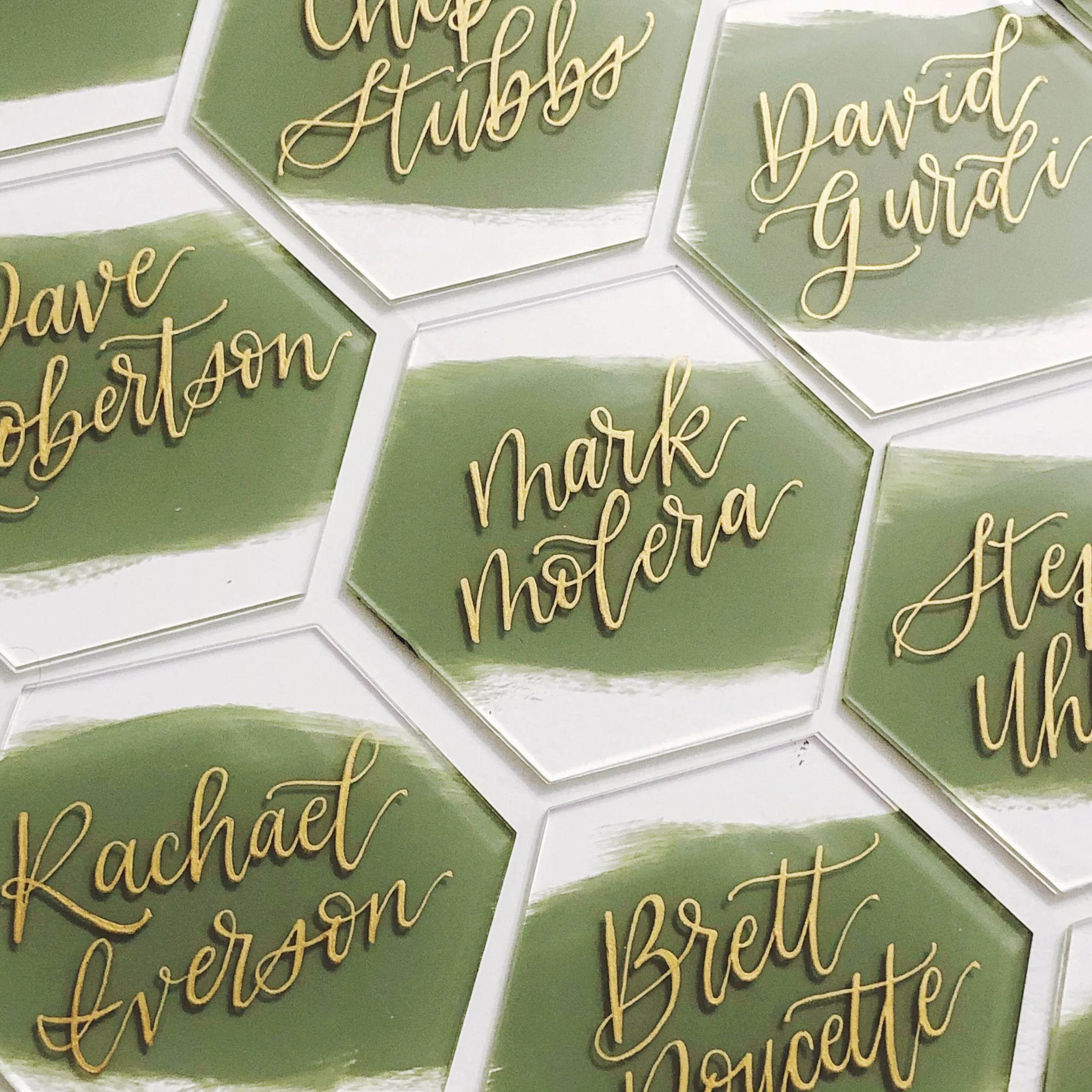 Modern sage painted back acrylic hexagon tile wedding escort cards featuring reflective metallic gold hand-lettering.