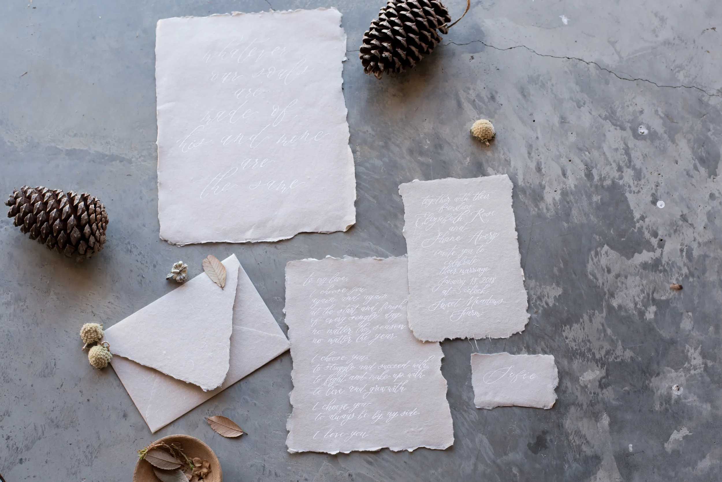 Inspire an organic, fine-art invitation design with textured handmade paper stationery. Featuring soft deckled edges, ethereal white ink calligraphy, and styled alongside fresh magnolia leaves and matching torn-flap envelopes, this suite is perfect f