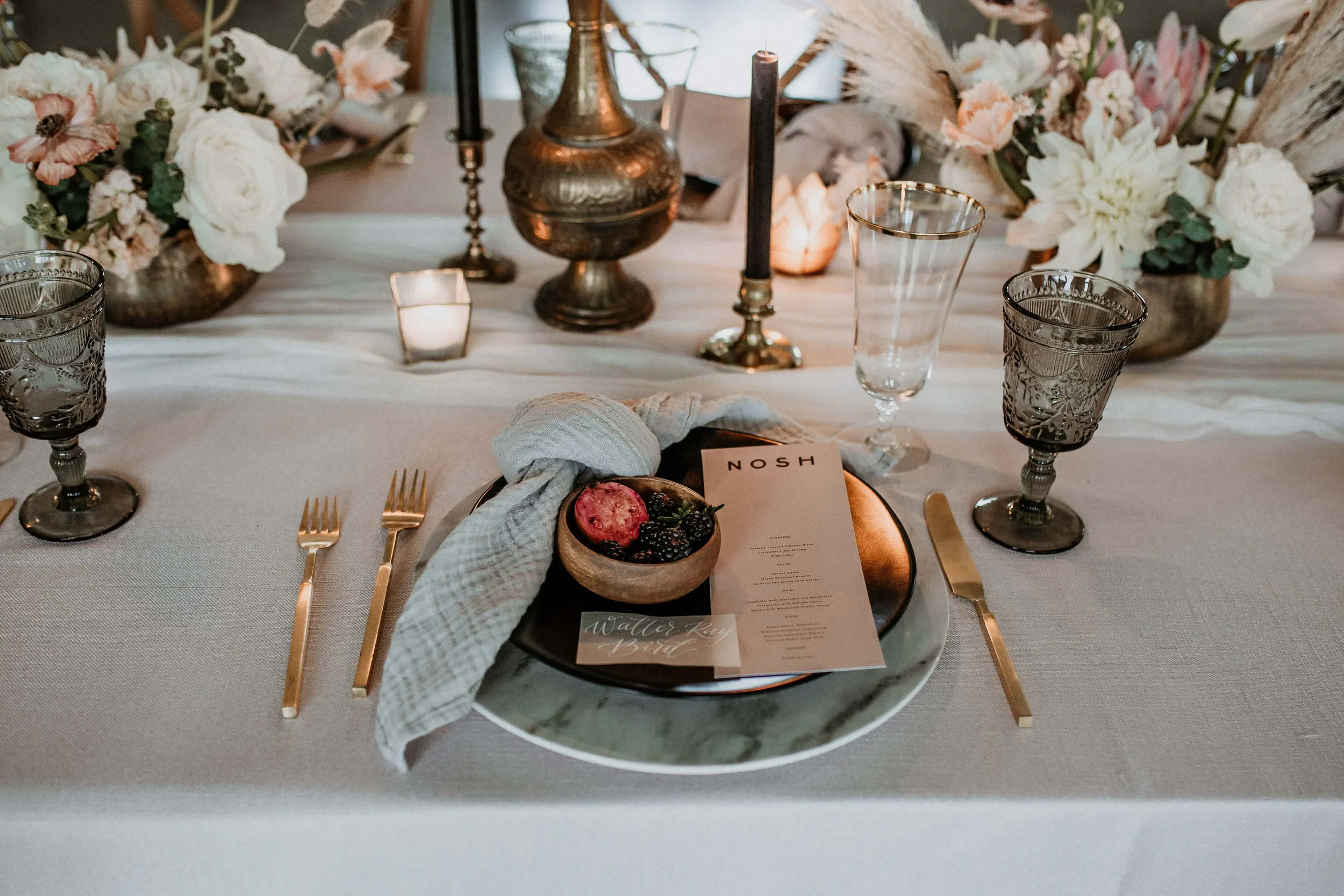 Fine art wedding table setting detailed with a vellum white ink calligraphy place card, blush dinner menu, sage linen napkin and a wooden bowl of sliced figs.