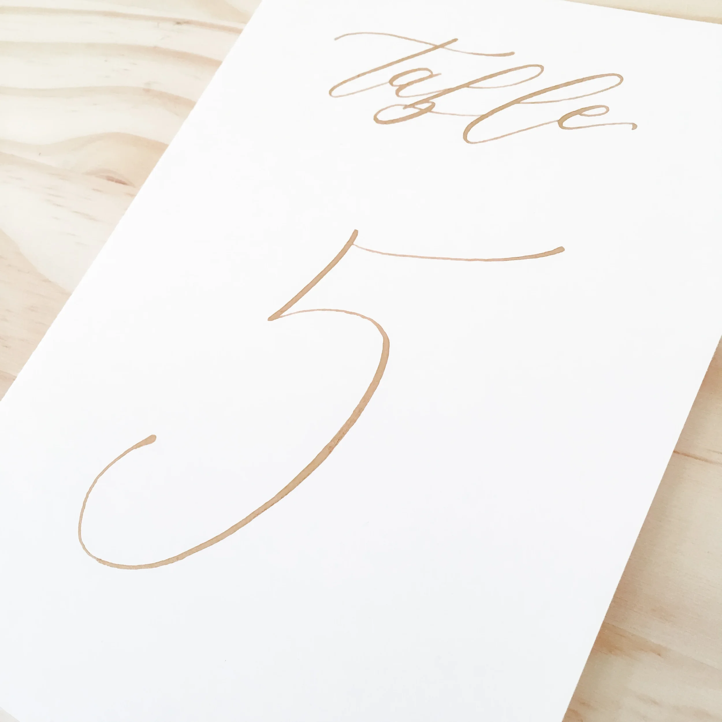 Ensure seamless reception navigation with clear, elegant script table numbers in gold ink calligraphy.