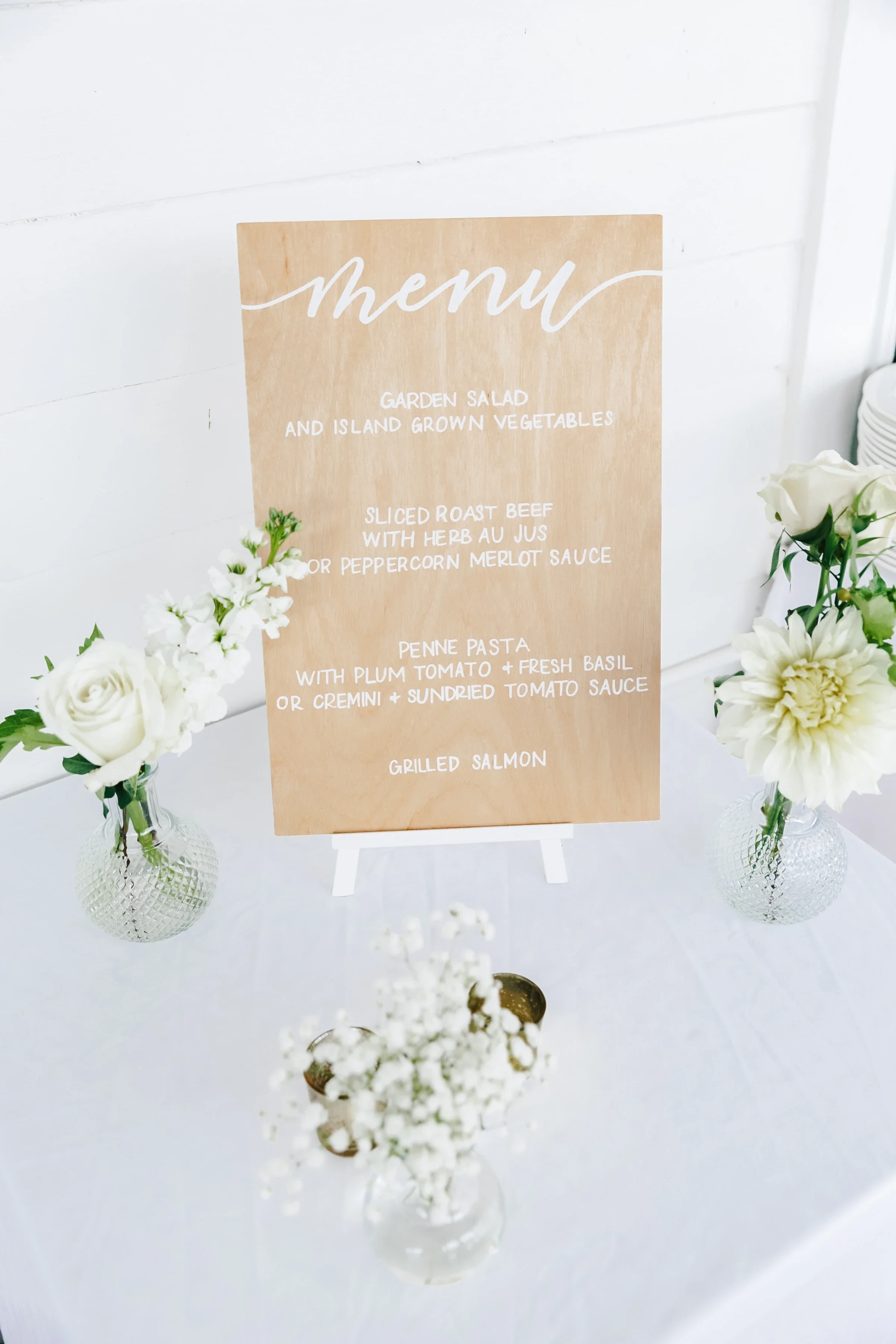 Modern minimalist wooden food menu sign displayed next to fresh white florals.