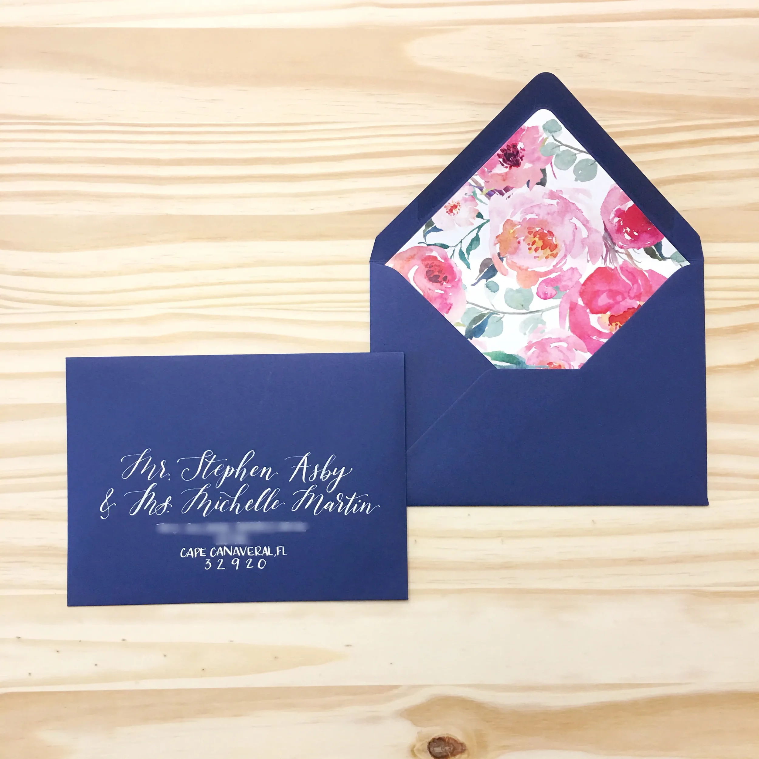 Deep navy blue invitation envelope opened to reveal a bright pink and red watercolor floral liner.