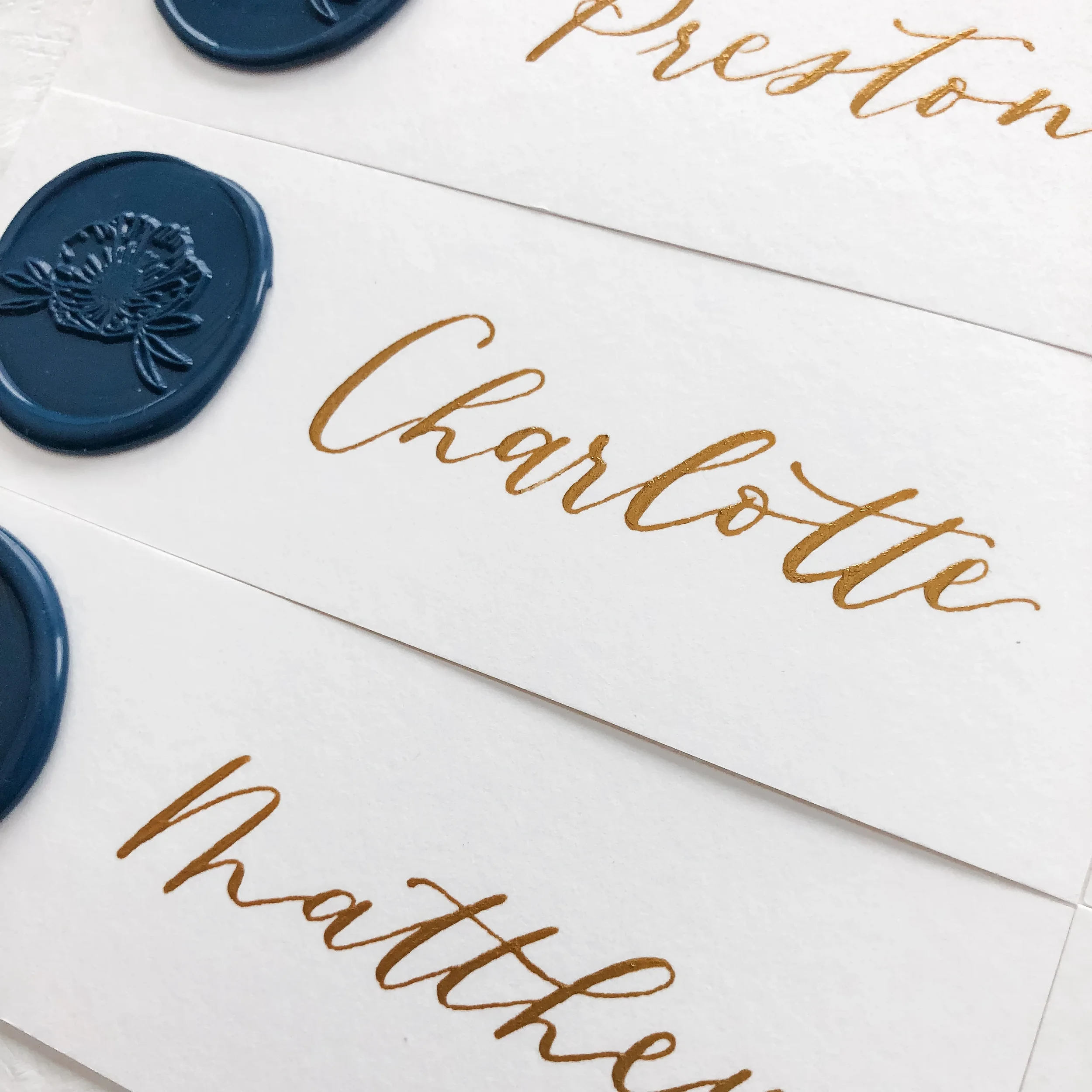 Elevate traditional seating indicators with fine-art paper escort strips. Each hand-torn strip features sweeping gold script lettering and is finished with an exquisite, deep navy blue floral wax seal stamp, adding a highly tactile, luxury element to