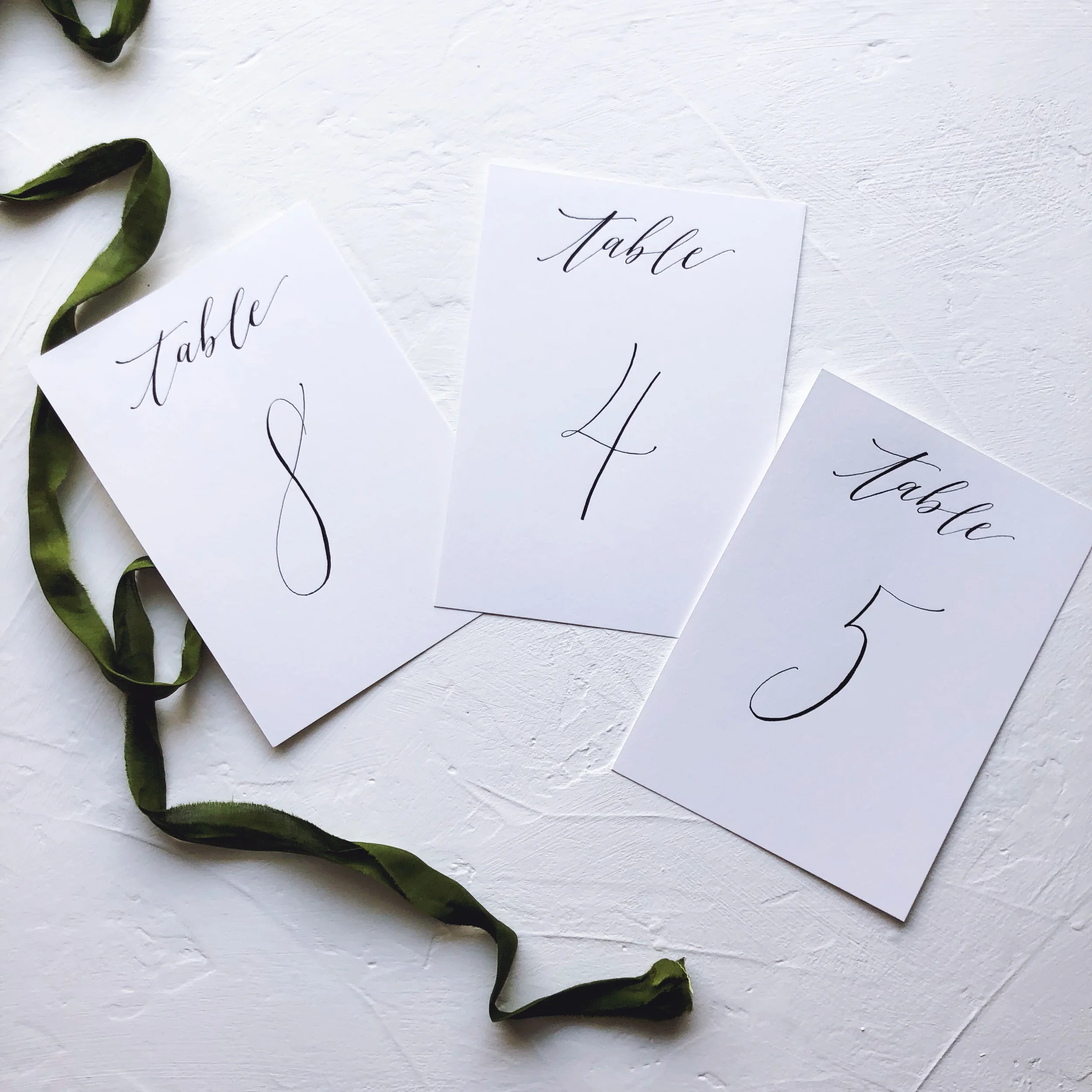 Traditional white cardstock table numbers written in classic black calligraphy.