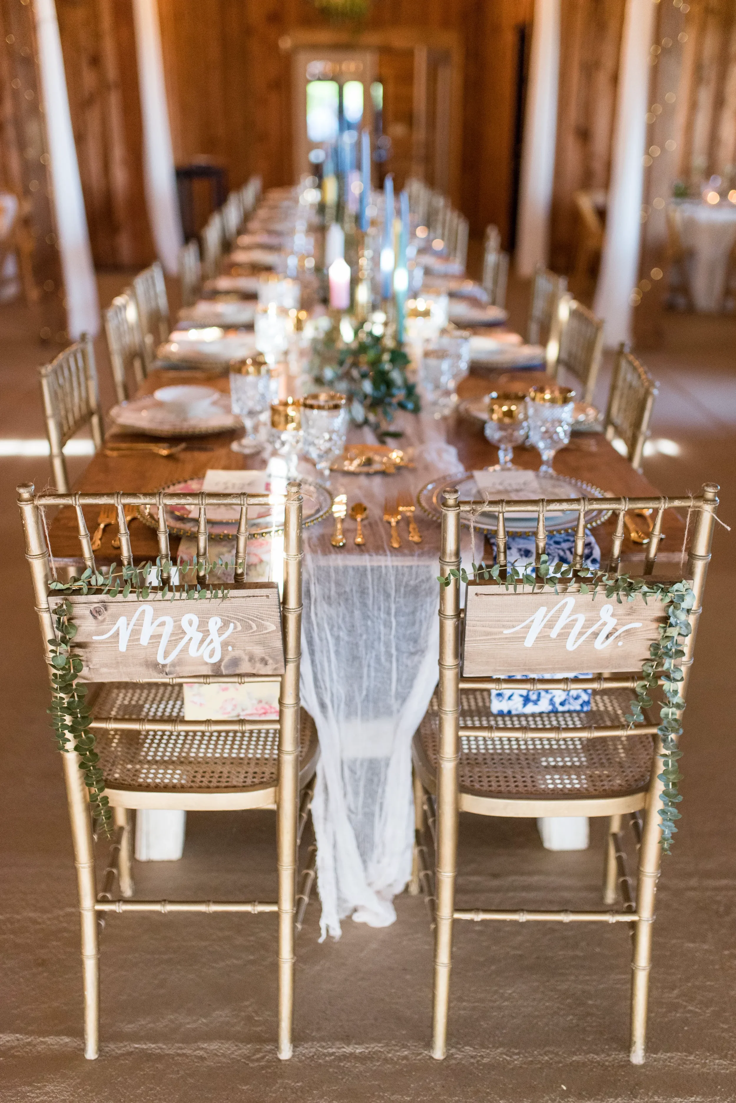 Pair of custom wooden Mr. and Mrs. calligraphy signs decorated with eucalyptus on gold chiavari chairs.