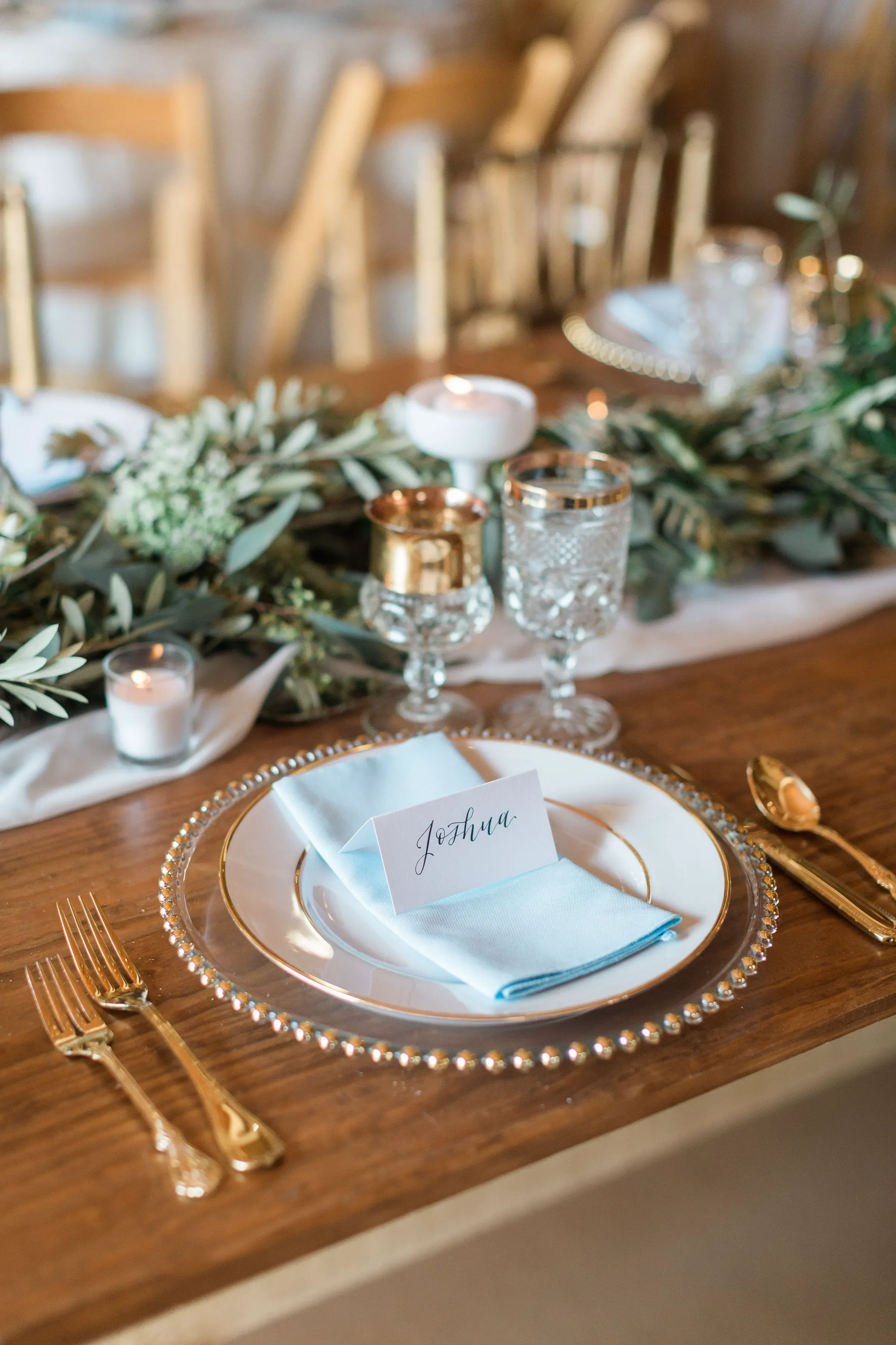 It is the fine details that truly welcome your guests. Give your reception tables a personalized, luxurious touch with custom handwritten script place cards. Beautifully paired here with soft blue textiles, elegant gold accents, crystal glassware, an