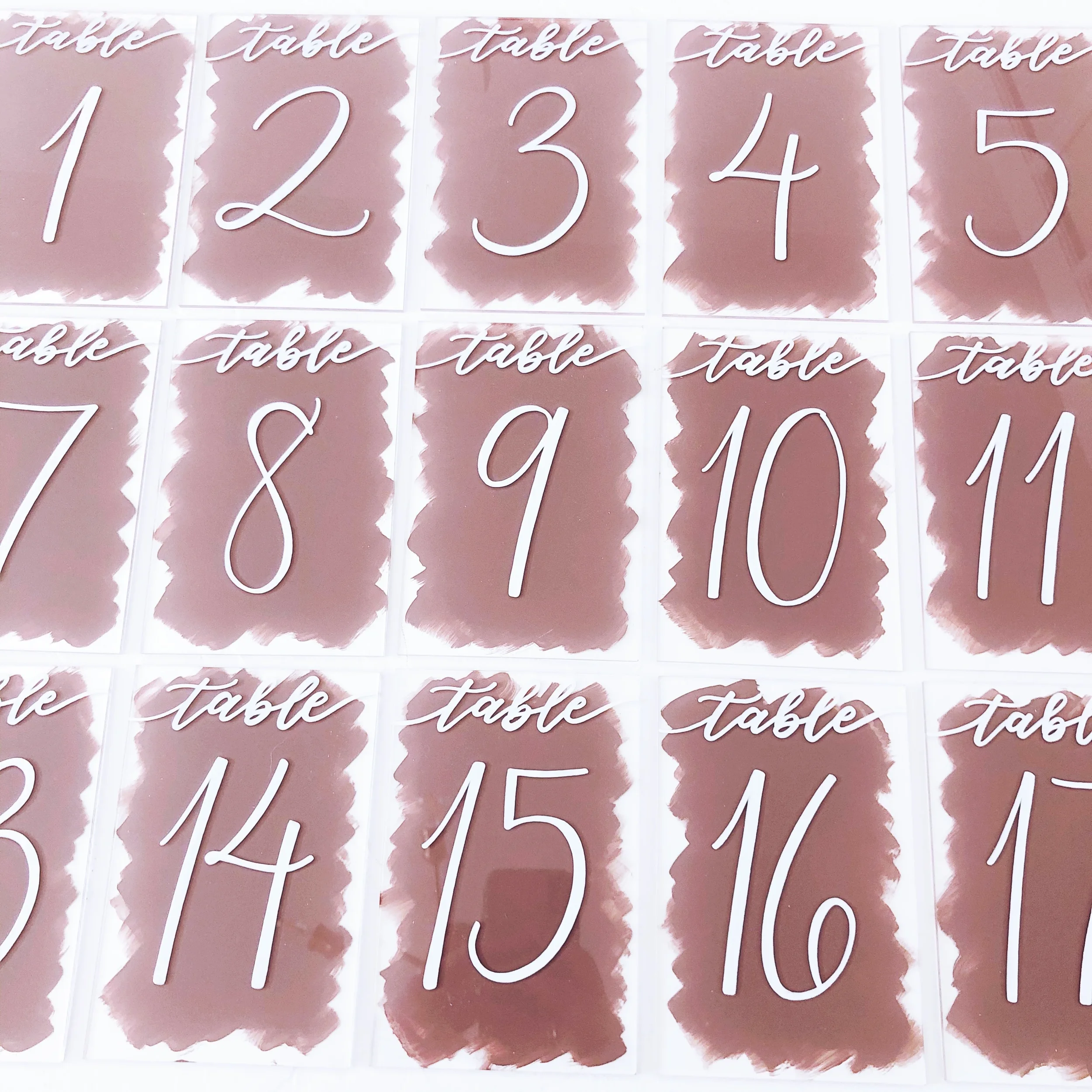 Clear lucite table number signs featuring a painted mauve background brushstroke and white calligraphy.