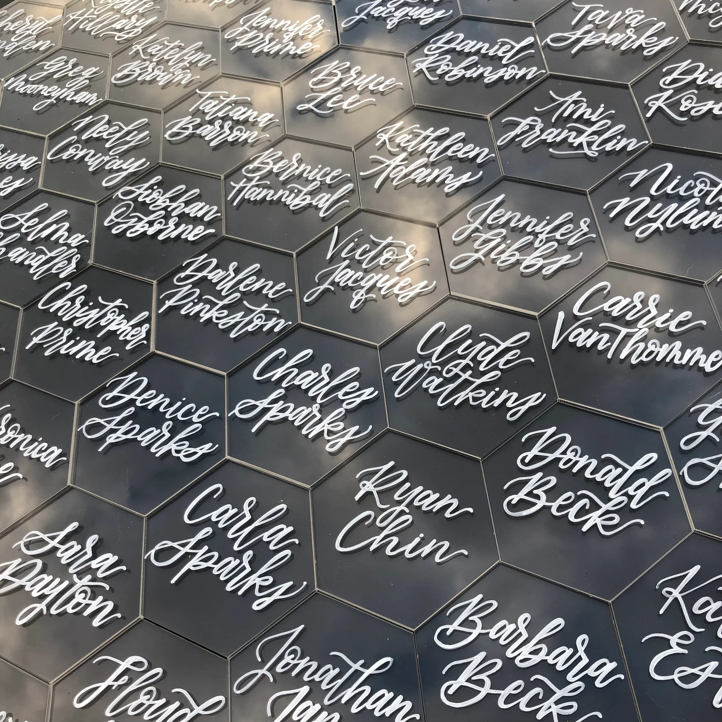 Clear acrylic hexagon place cards with white hand lettered names for a modern wedding table setting.