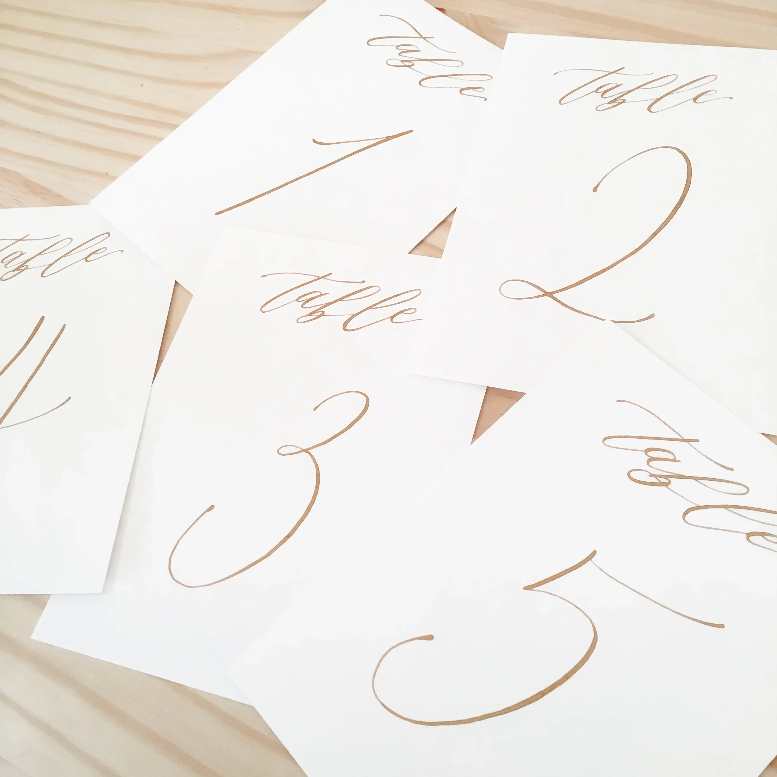 Gold calligraphy table numbers on white cardstock paper.