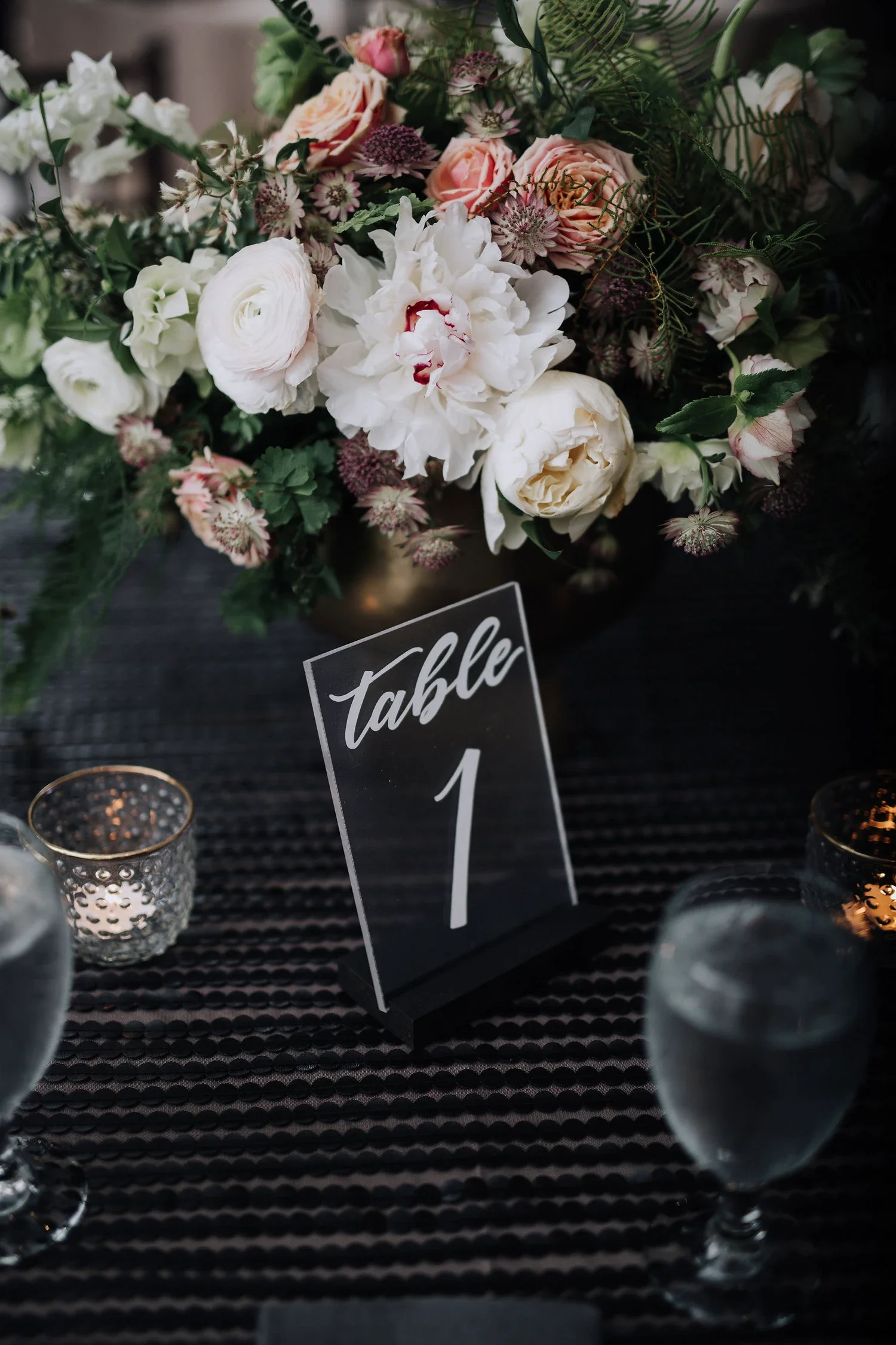 Clear acrylic table number in white hand-lettering on a black stand for a moody modern wedding.
