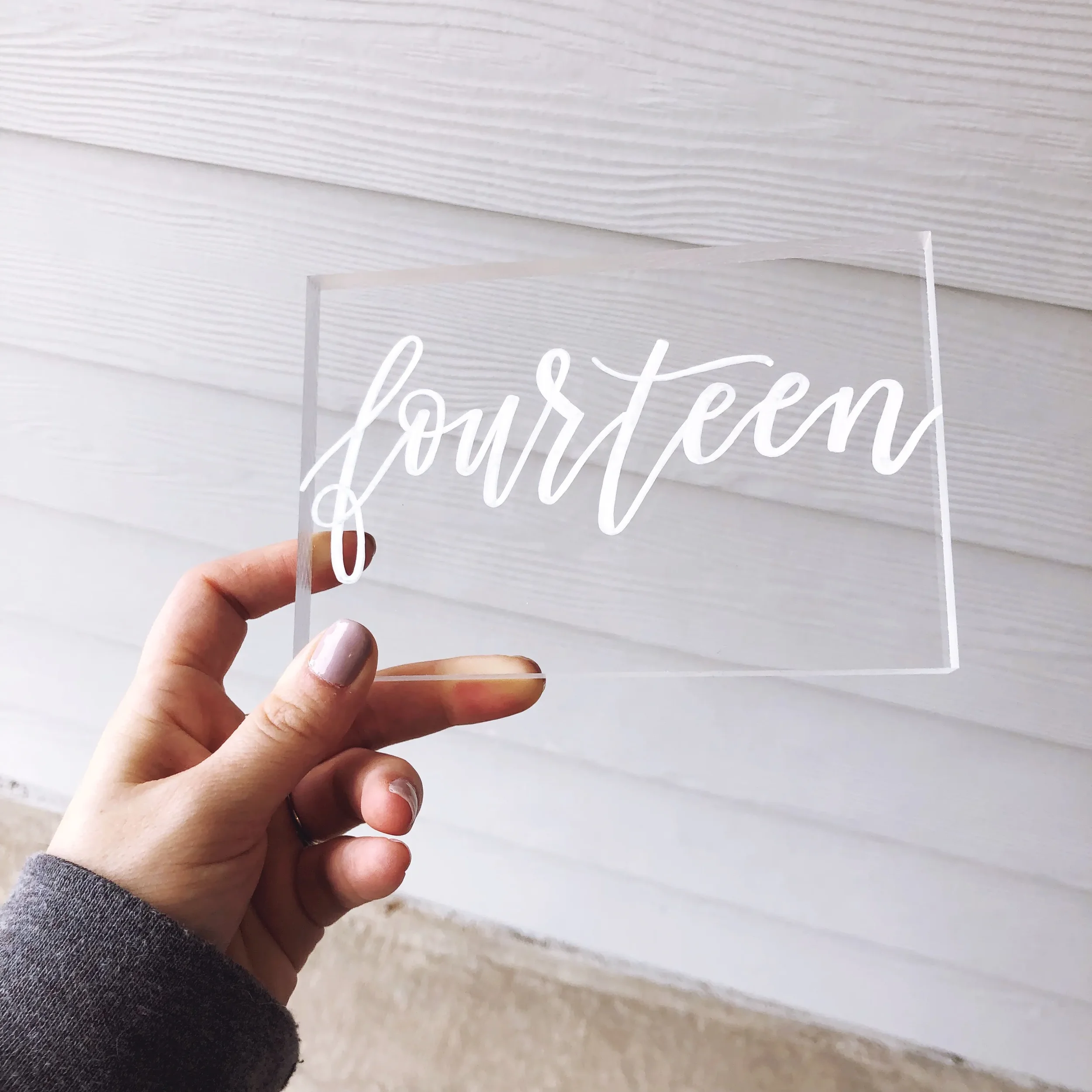 Clear acrylic table number block with white hand-lettered calligraphy.