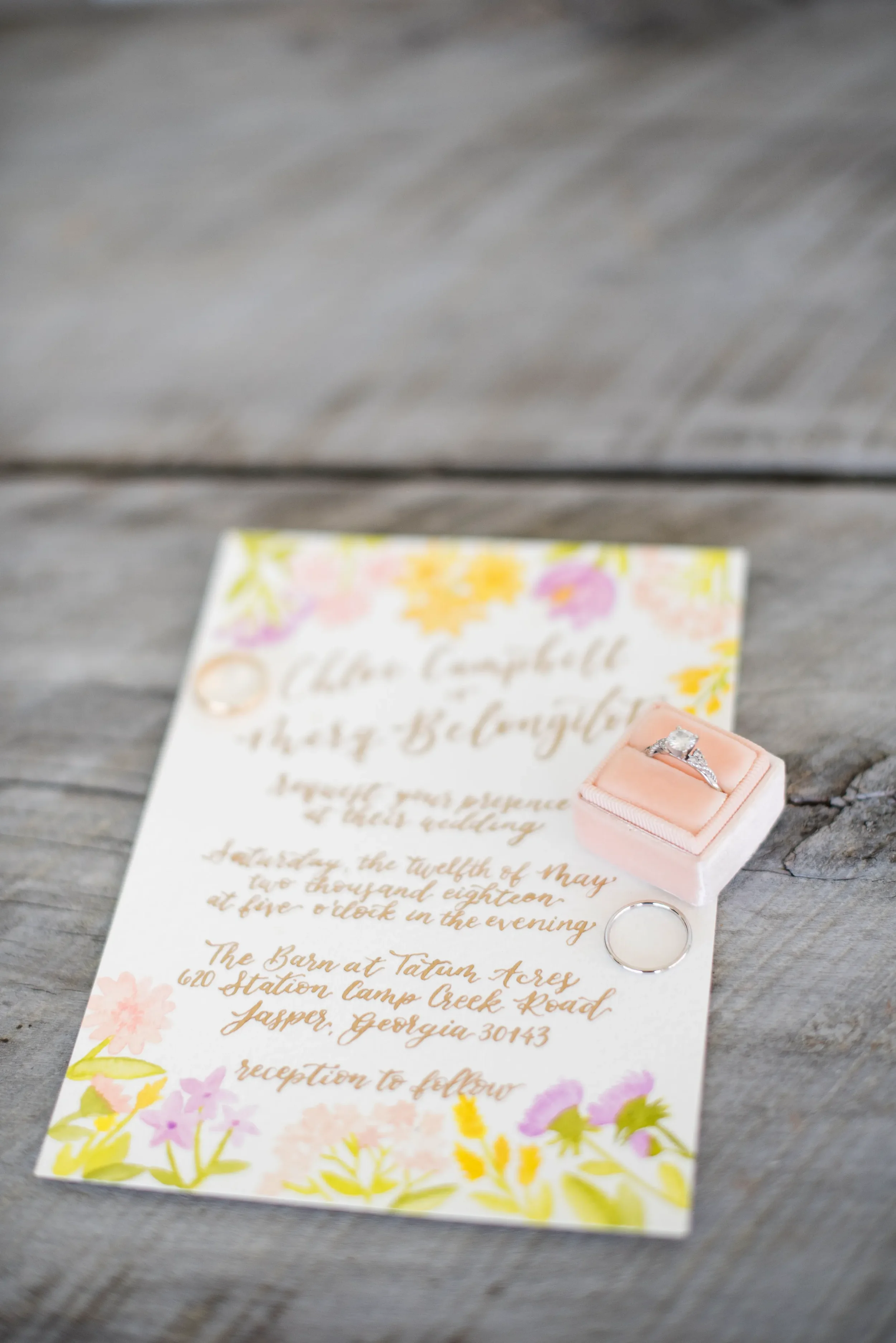 Flat lay of custom day of wedding invitations with vibrant watercolor flowers and gold calligraphy script.