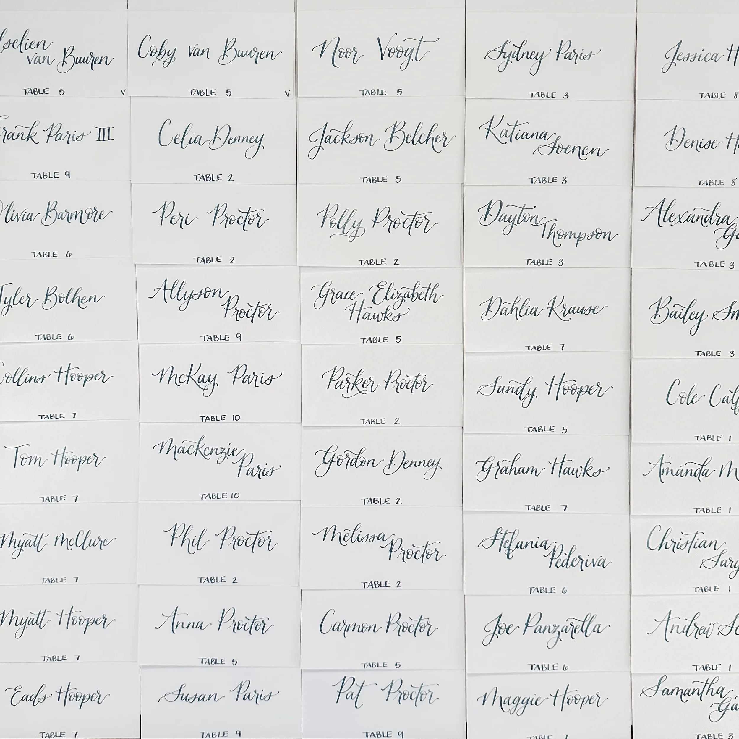 Large grid array of white folded wedding escort cards calligraphed in soft dusty blue script ink.