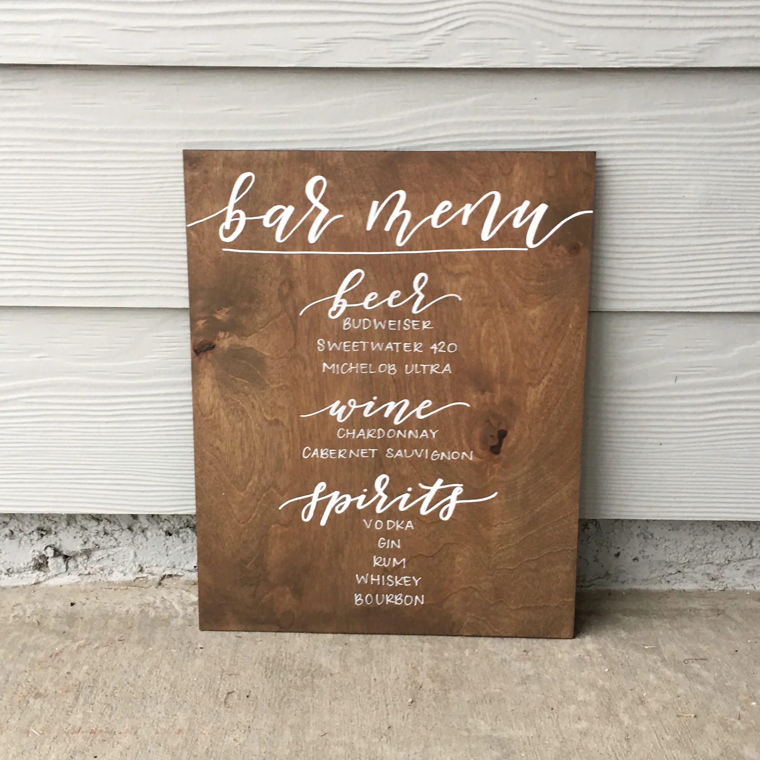 Hand-lettered wooden reception drink menu board listing beer, wine, and spirits.